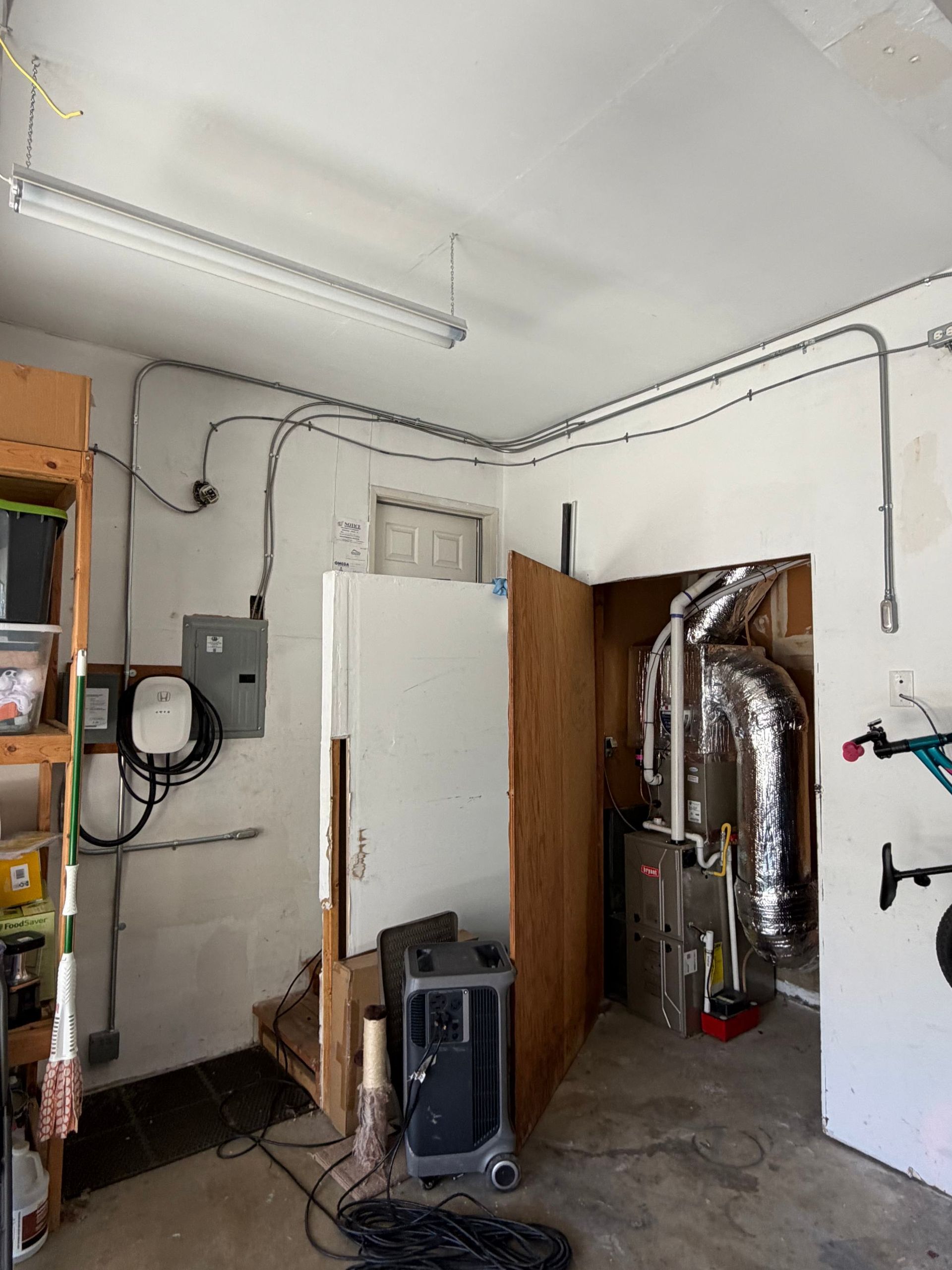 Garage interior with white cabinets, exposed ducting, shelving, and a portable heater or AC unit.