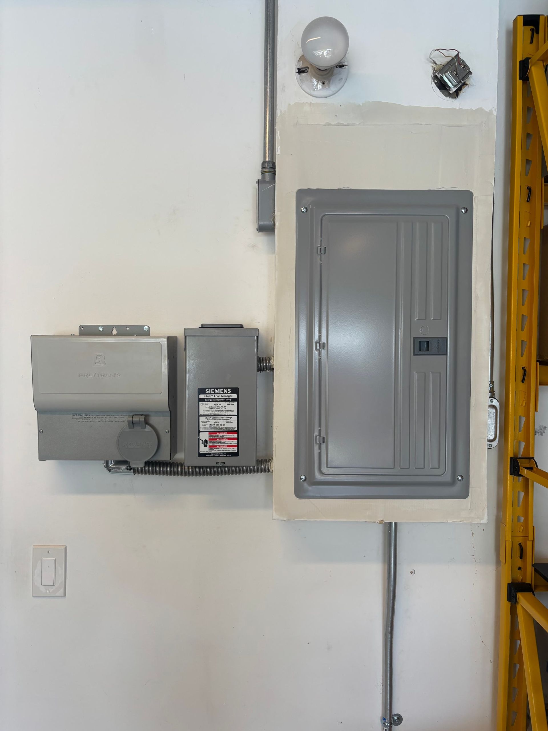 Electrical panels mounted on a white wall with conduit and a small light fixture nearby