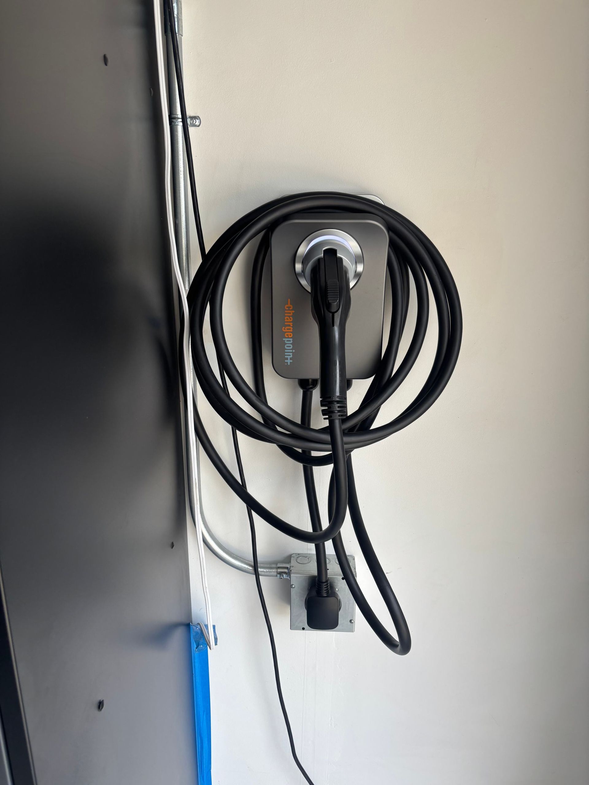 Coiled black charging cable mounted on a white wall beside a dark surface.