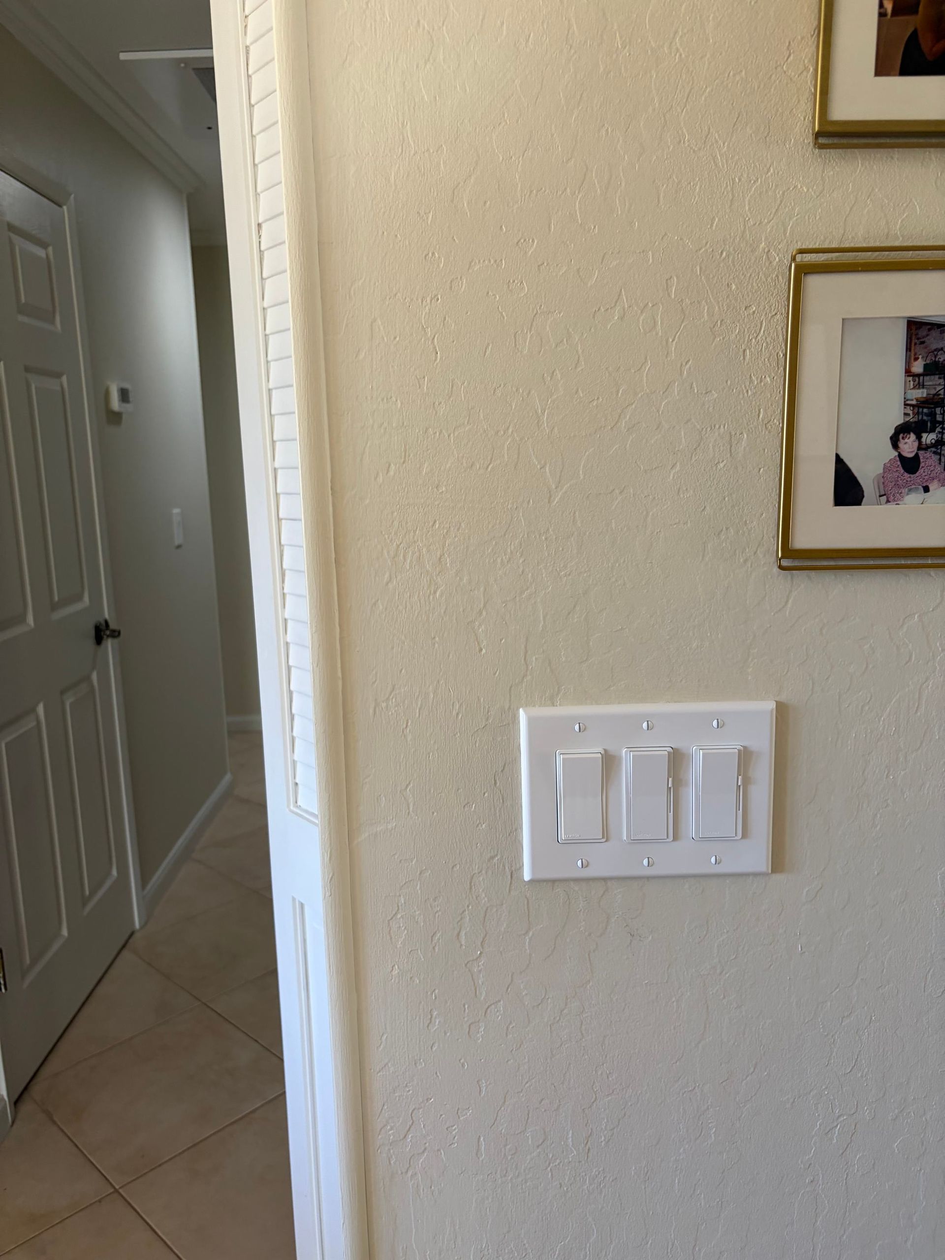 Hallway wall with white light switch and framed photos on beige wall