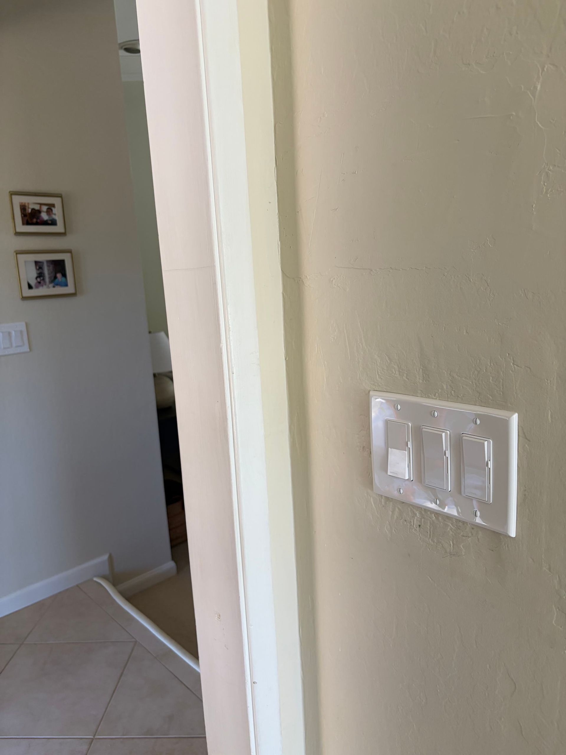Hallway corner with beige walls, tile floor, and a white light switch plate near a doorway.