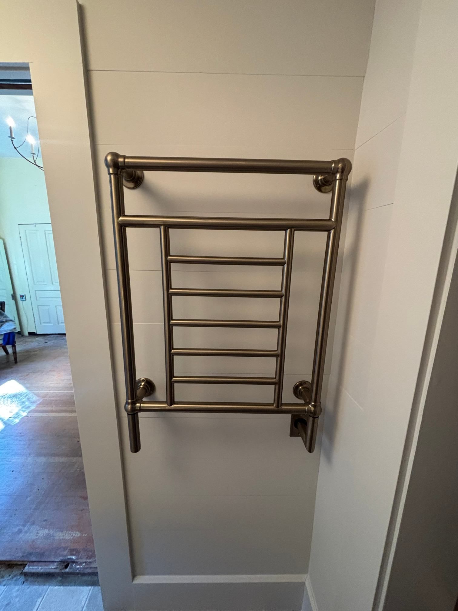 Wall-mounted metal towel rack on a light gray wall beside a doorway.