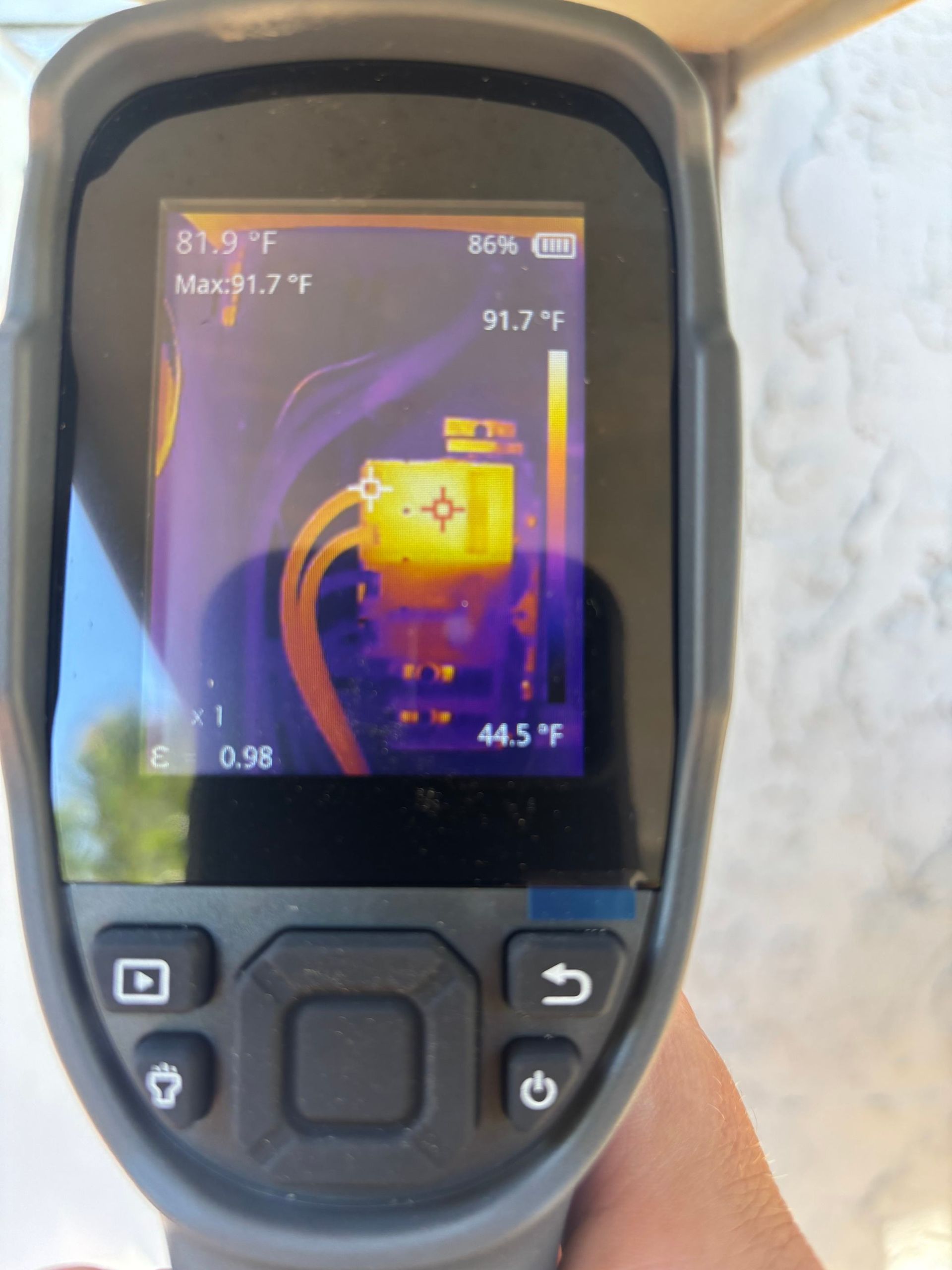 Handheld thermal camera showing a bright yellow heat source on a dark screen
