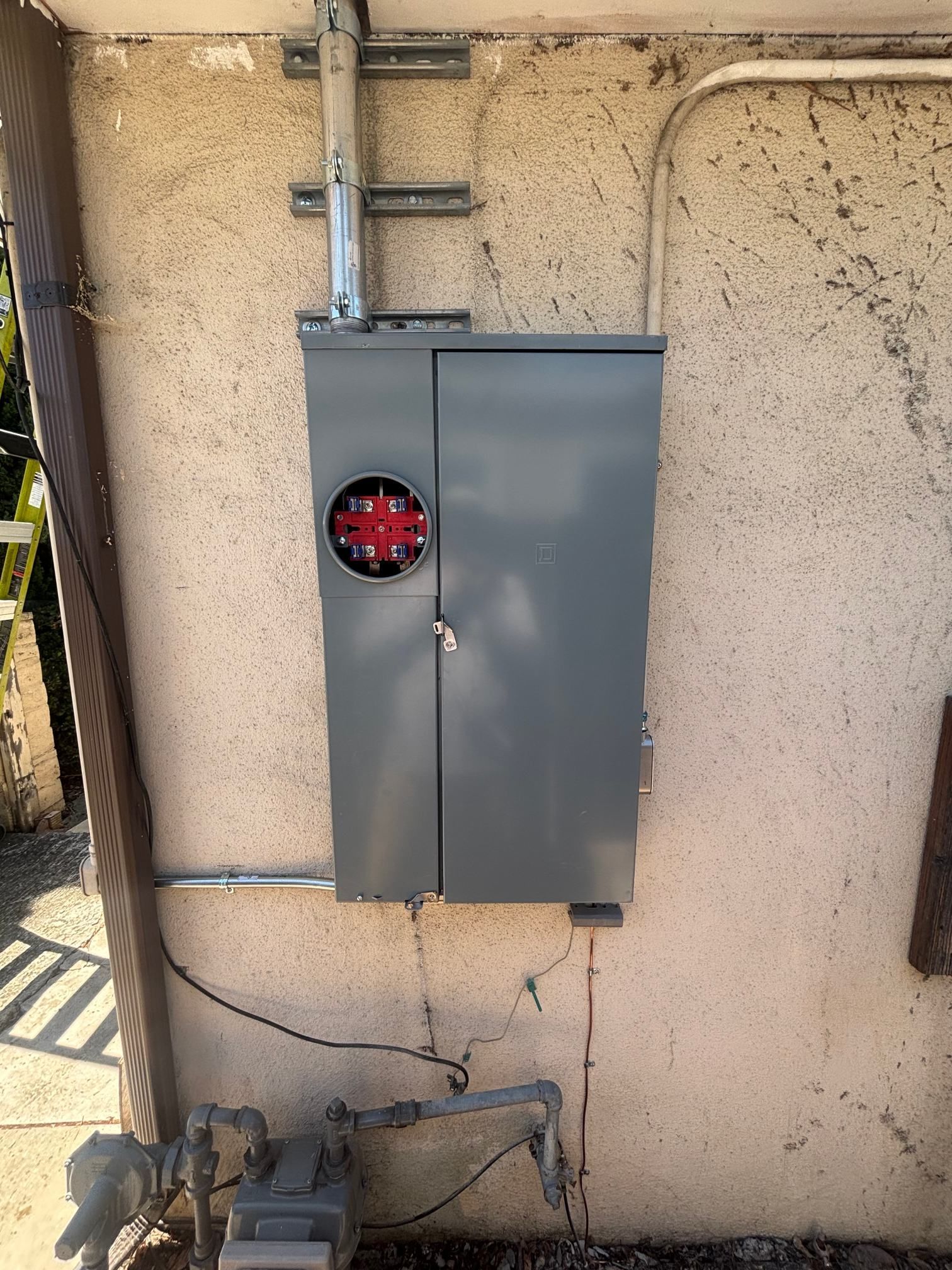 Gray electrical breaker box mounted on a stucco wall with conduit and cables attached