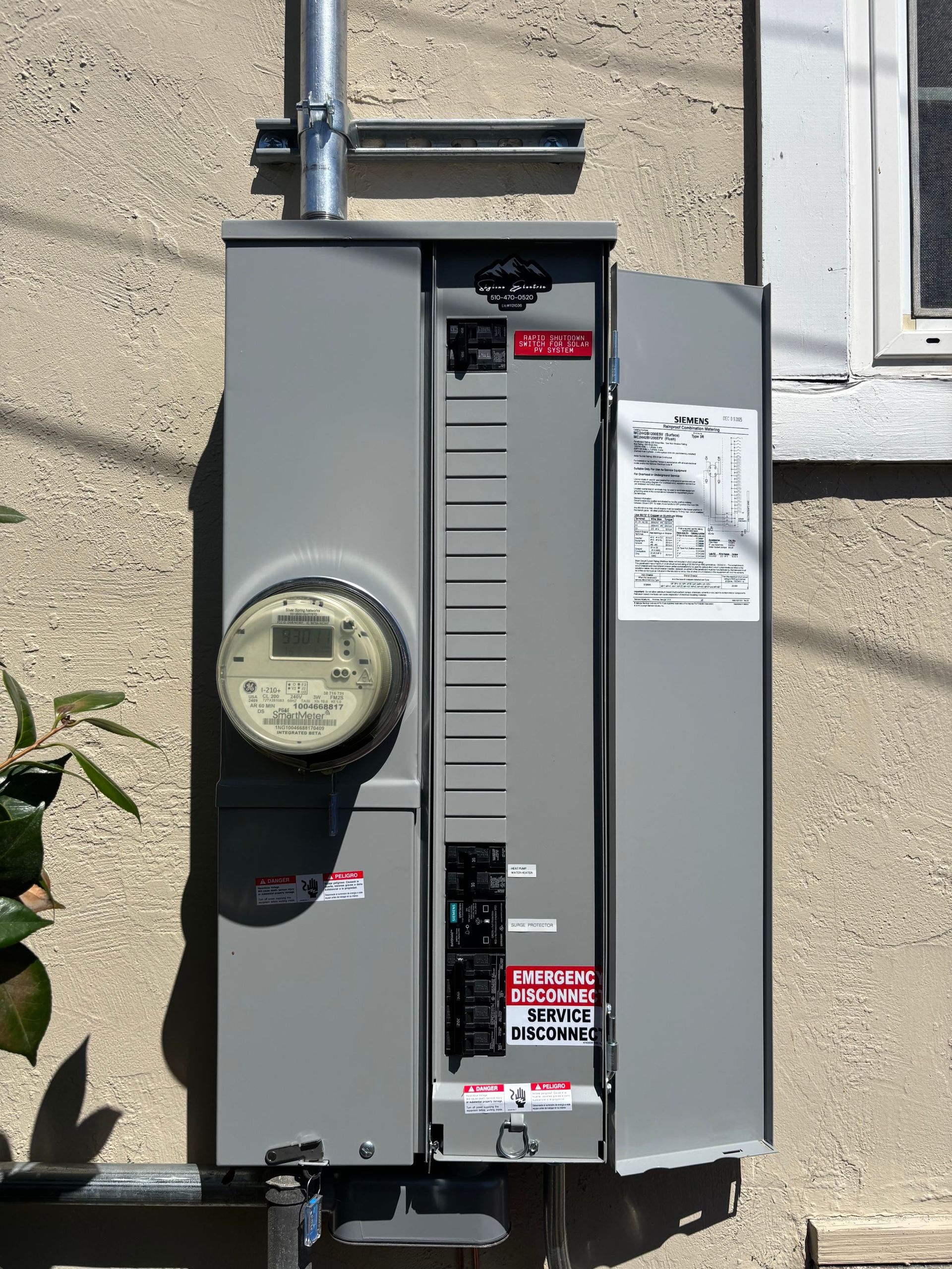 Gray outdoor electrical meter panel mounted on a beige stucco wall with conduit above it