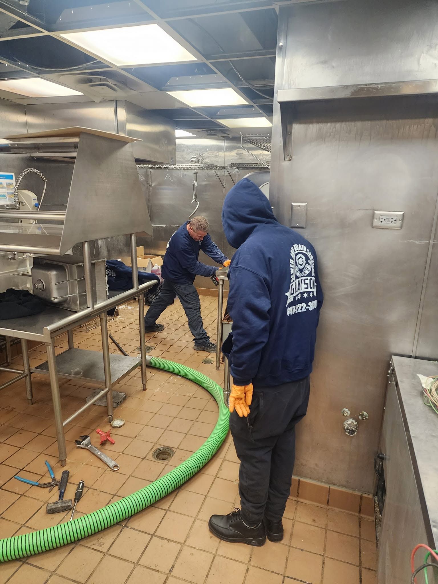 Hands installing a gray garbage disposal under a kitchen sink with exposed pipes