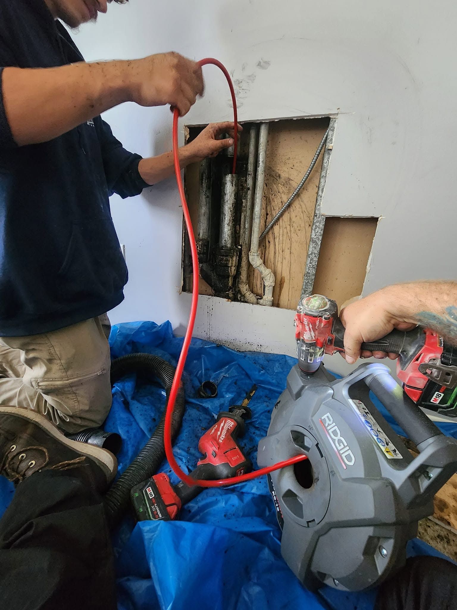 Plumber tightening a blue water filter housing under a sink with a wrench