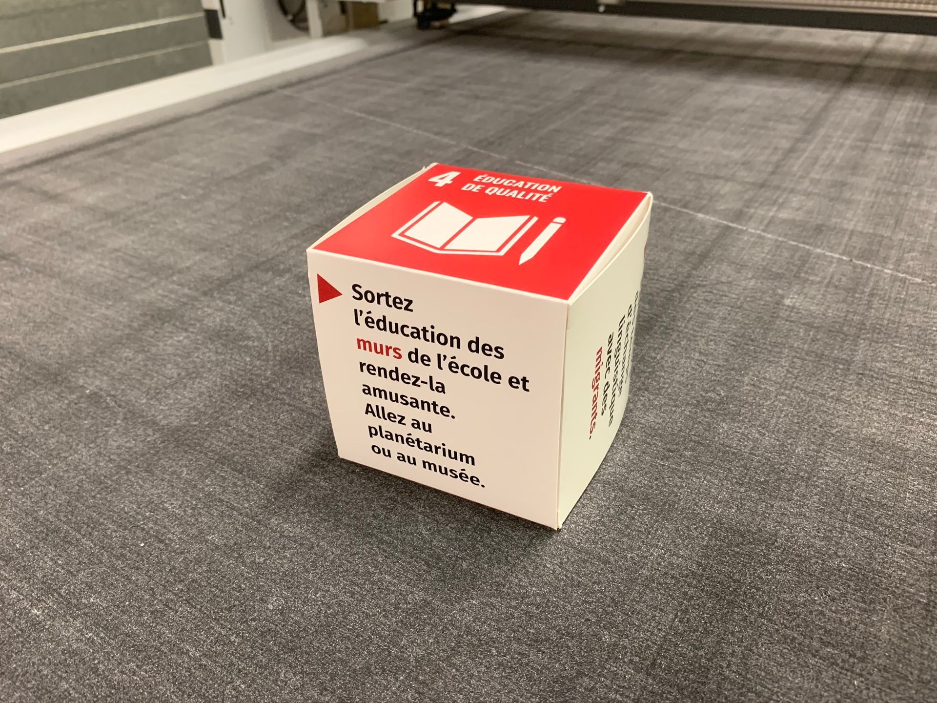 Une boîte blanche avec un couvercle rouge est posée sur le sol.