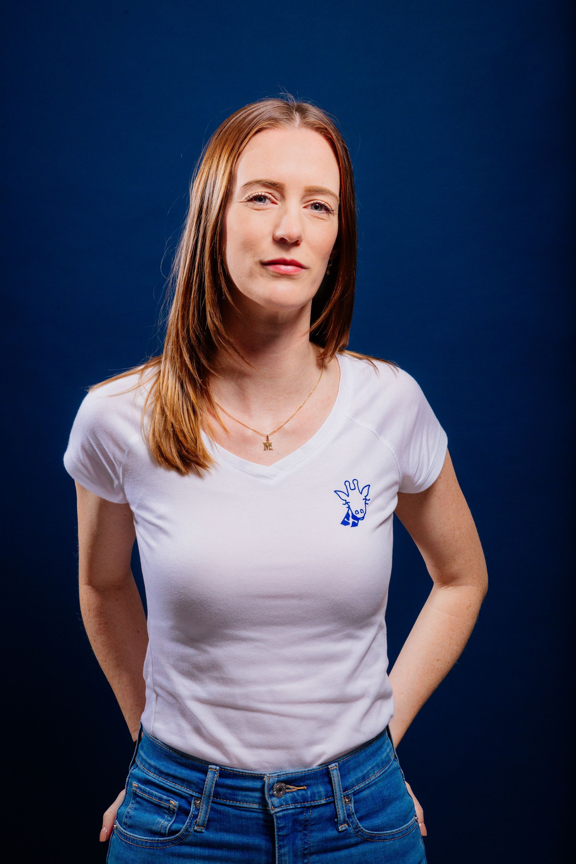 Une femme portant un t-shirt blanc et un jean bleu se tient debout devant un fond bleu.
