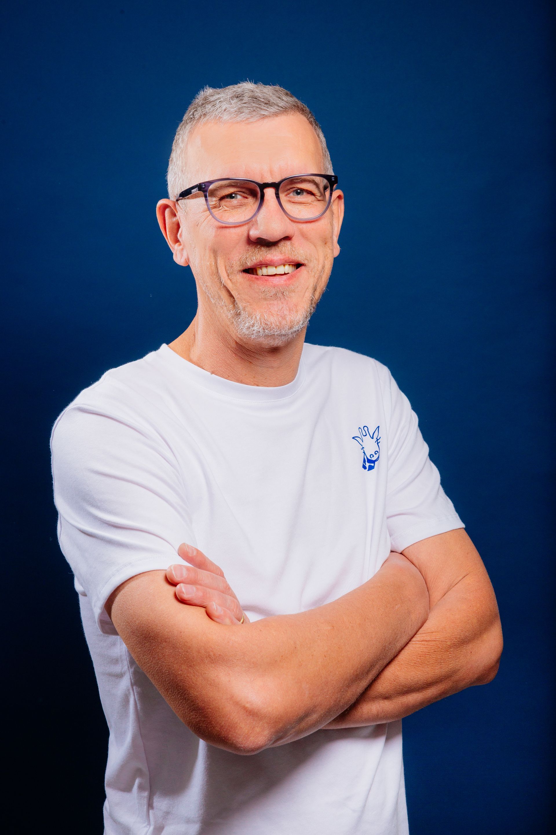Un homme portant des lunettes et une chemise blanche est debout avec les bras croisés.