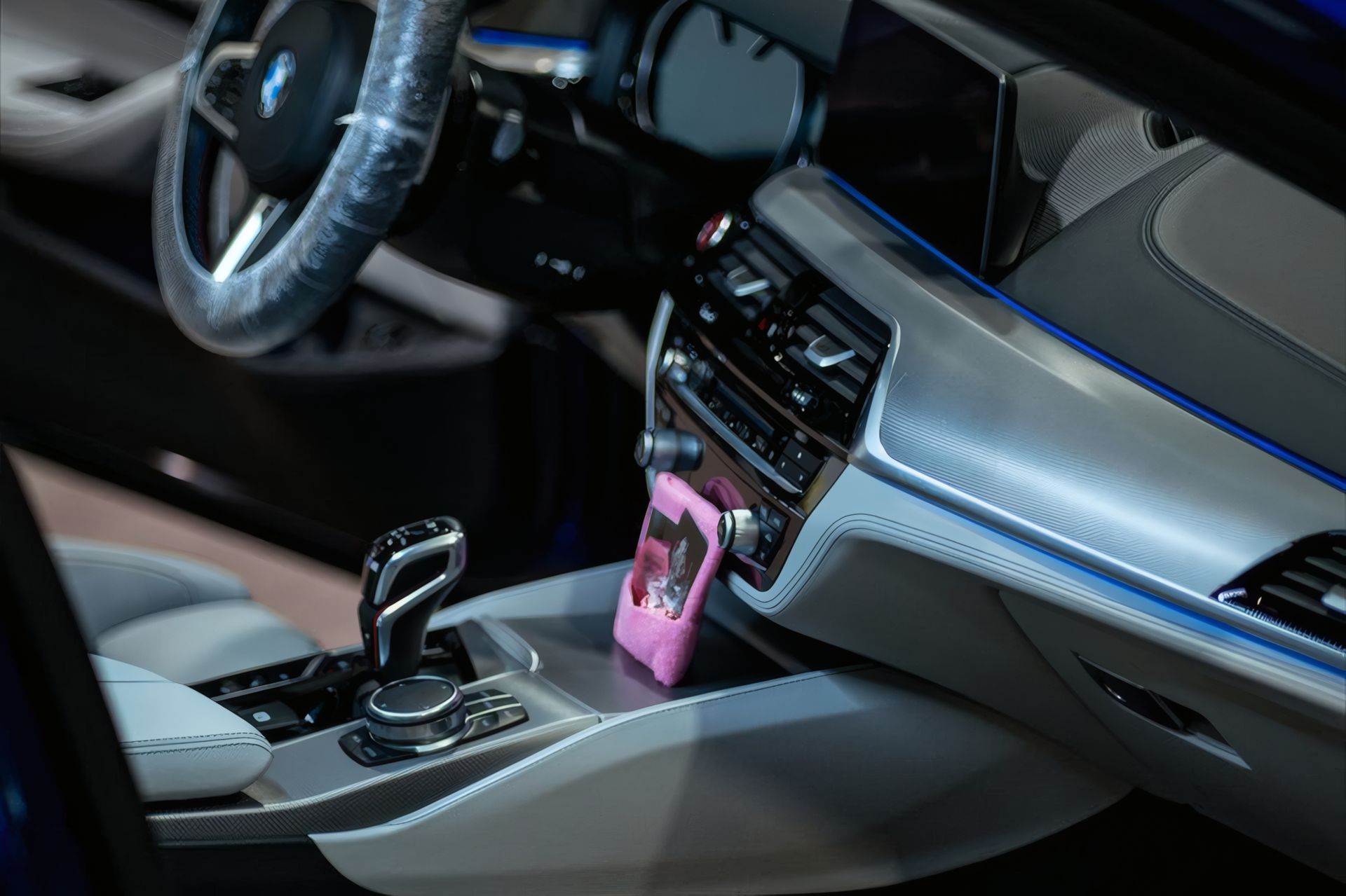 Car interior with steering wheel, center console, gear shifter, and a pink item on the dashboard