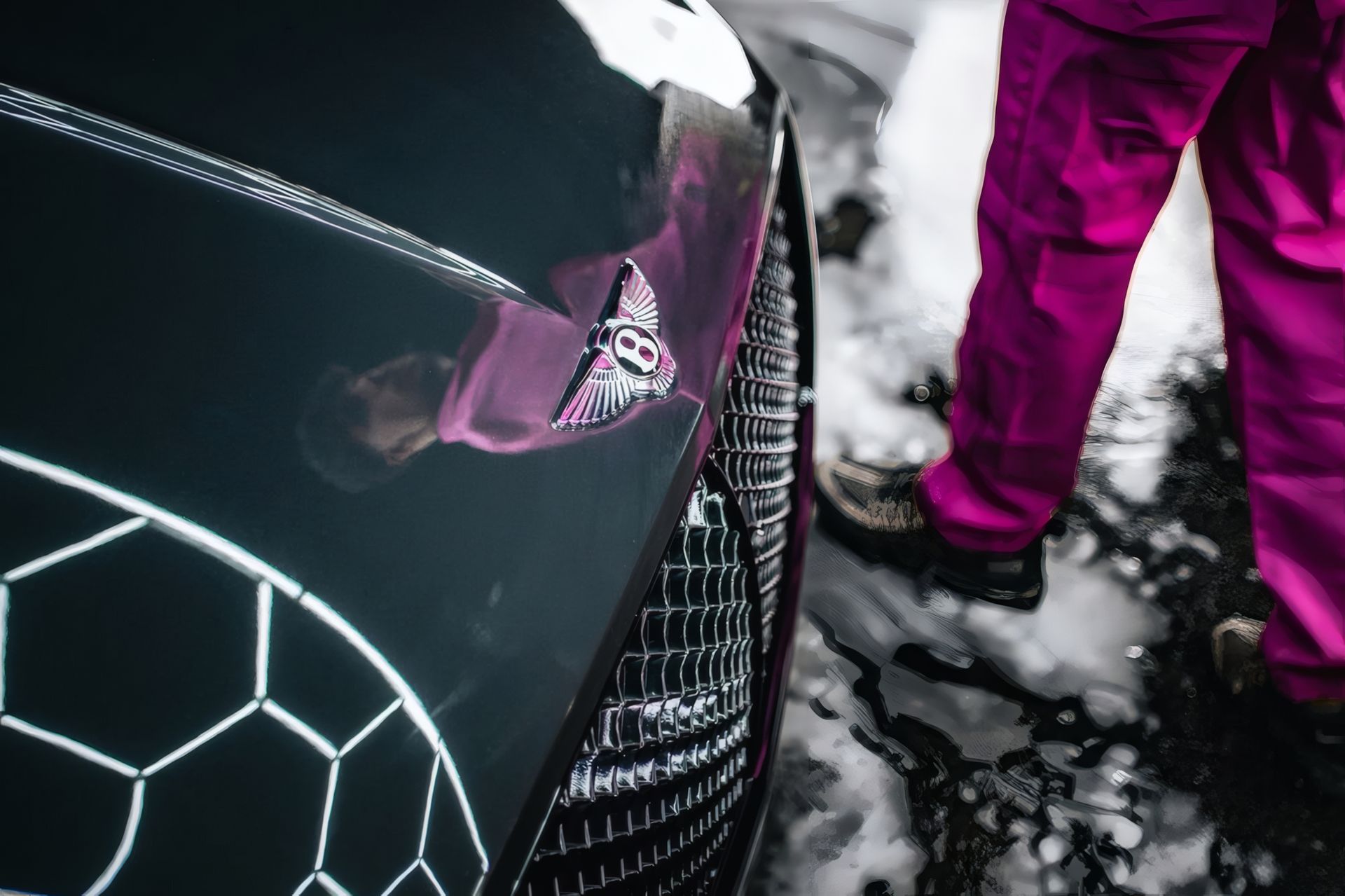 Close-up of a black car with a pink accent and a person’s magenta pants standing in soap suds.