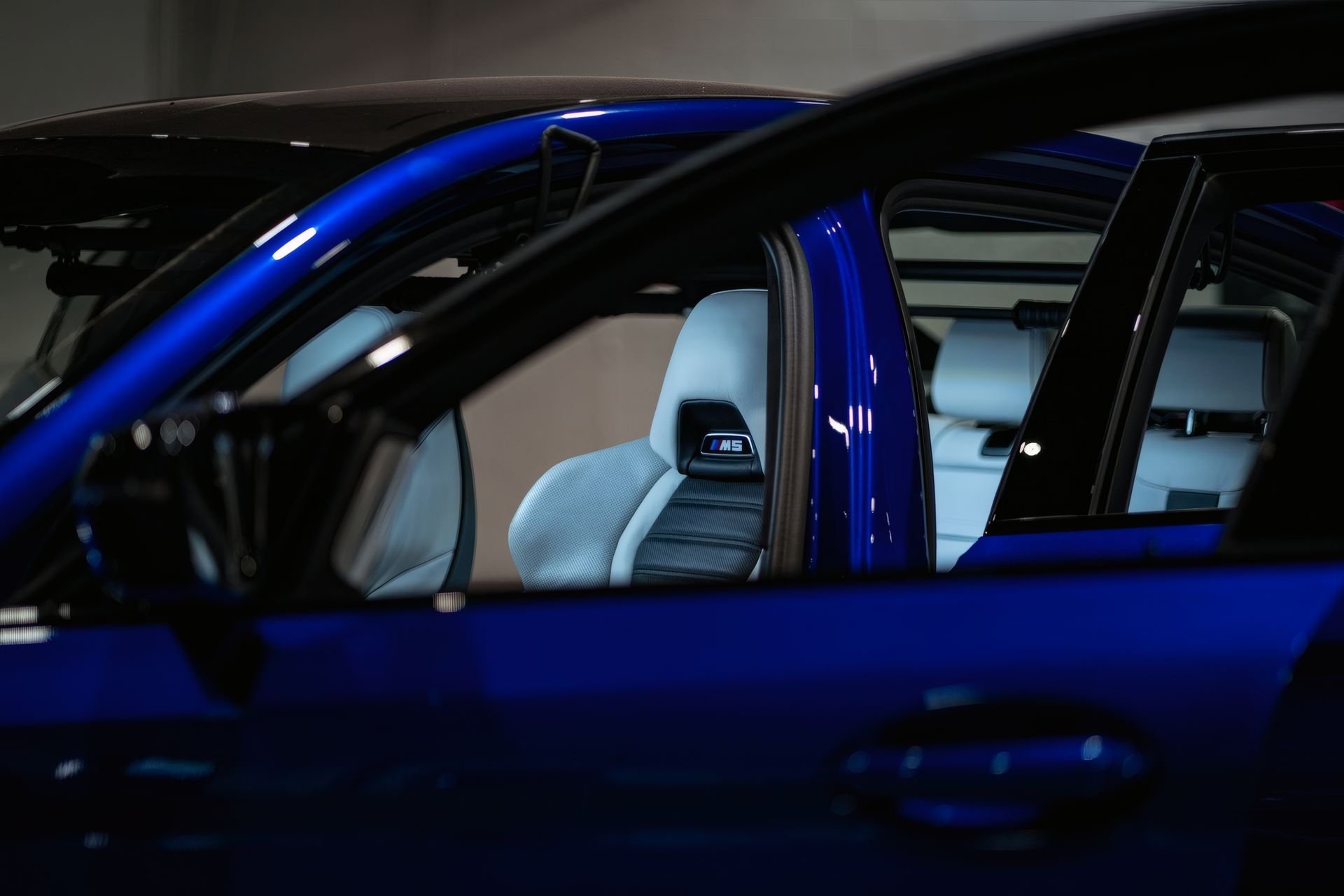 Blue car interior seen through open door, with gray seats visible in a dim garage.