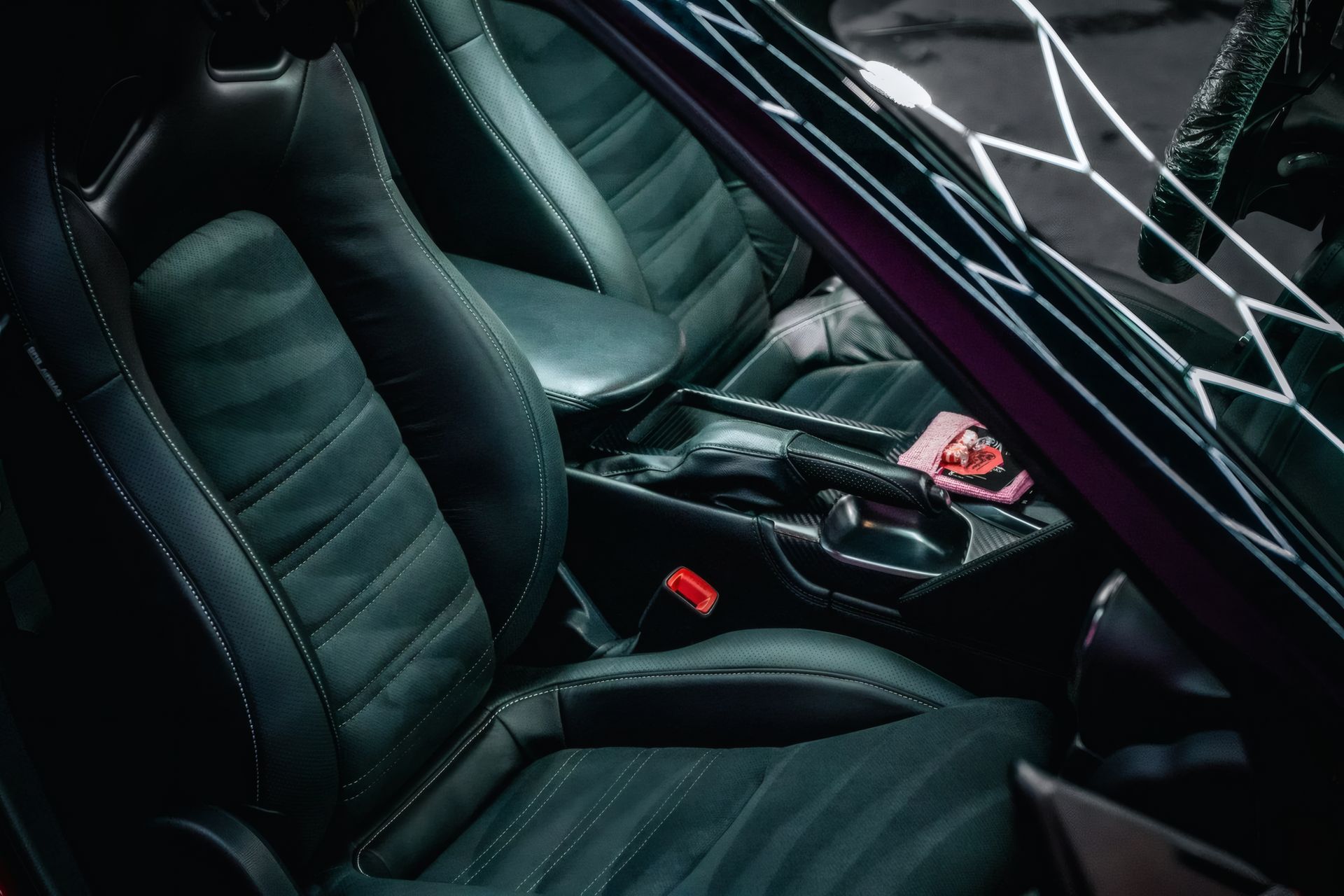 Black leather car interior with front seats, center console, and red accessories on the console