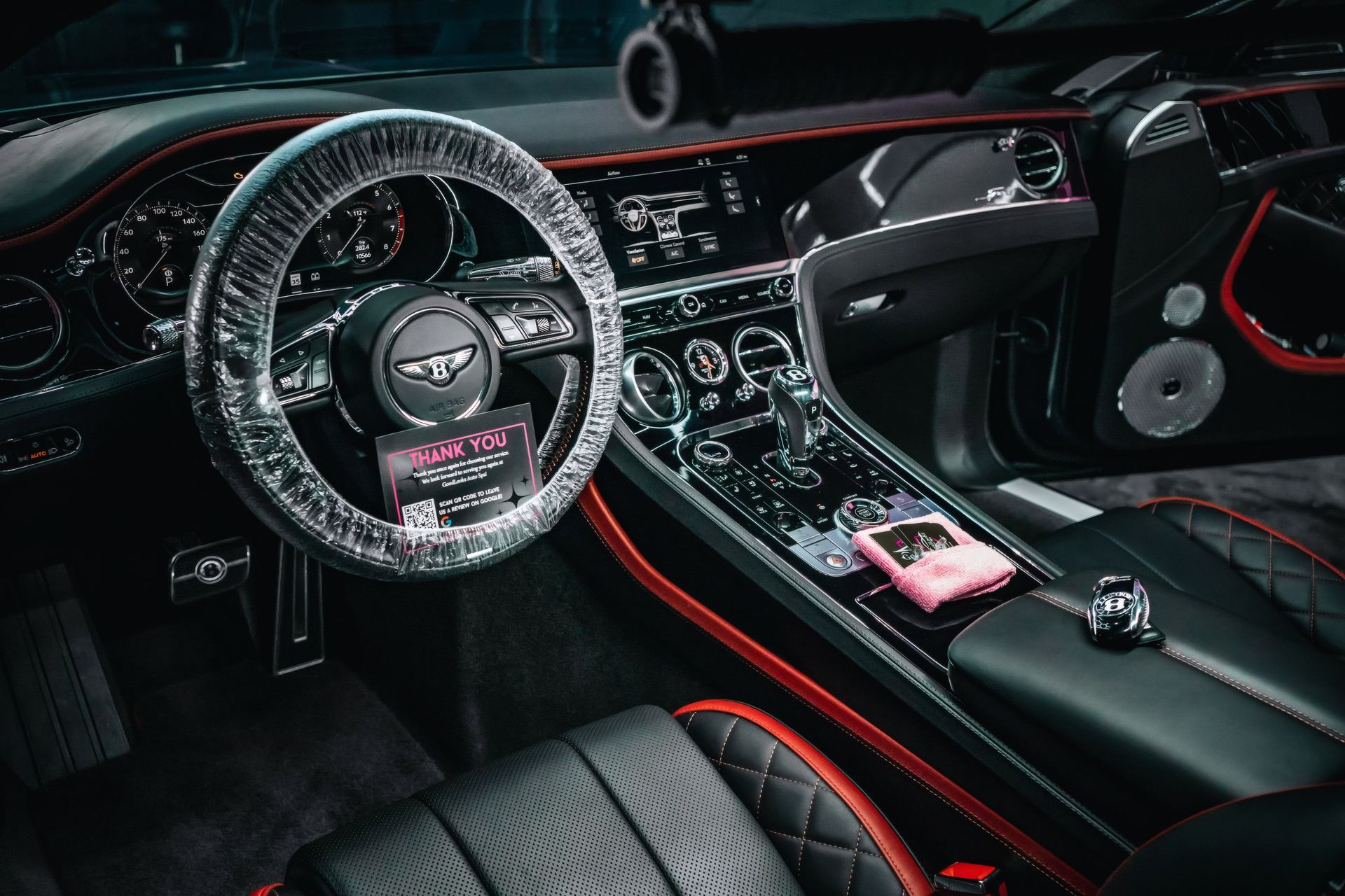 Custom black sports car interior with orange accents and a plastic wrapped steering wheel, dashboard, and seat trim