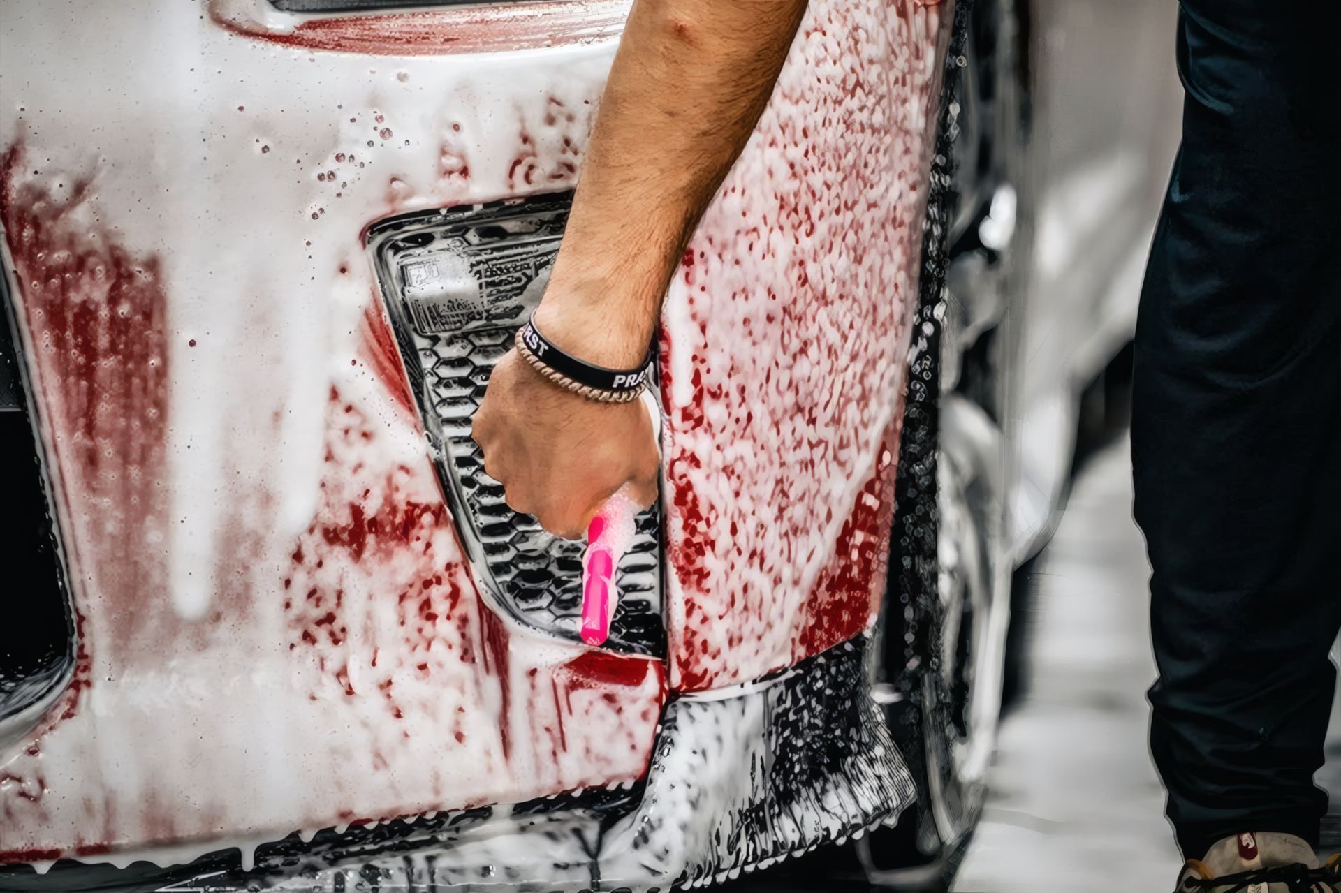 Hand washing a red car with soapy foam and a pink sponge