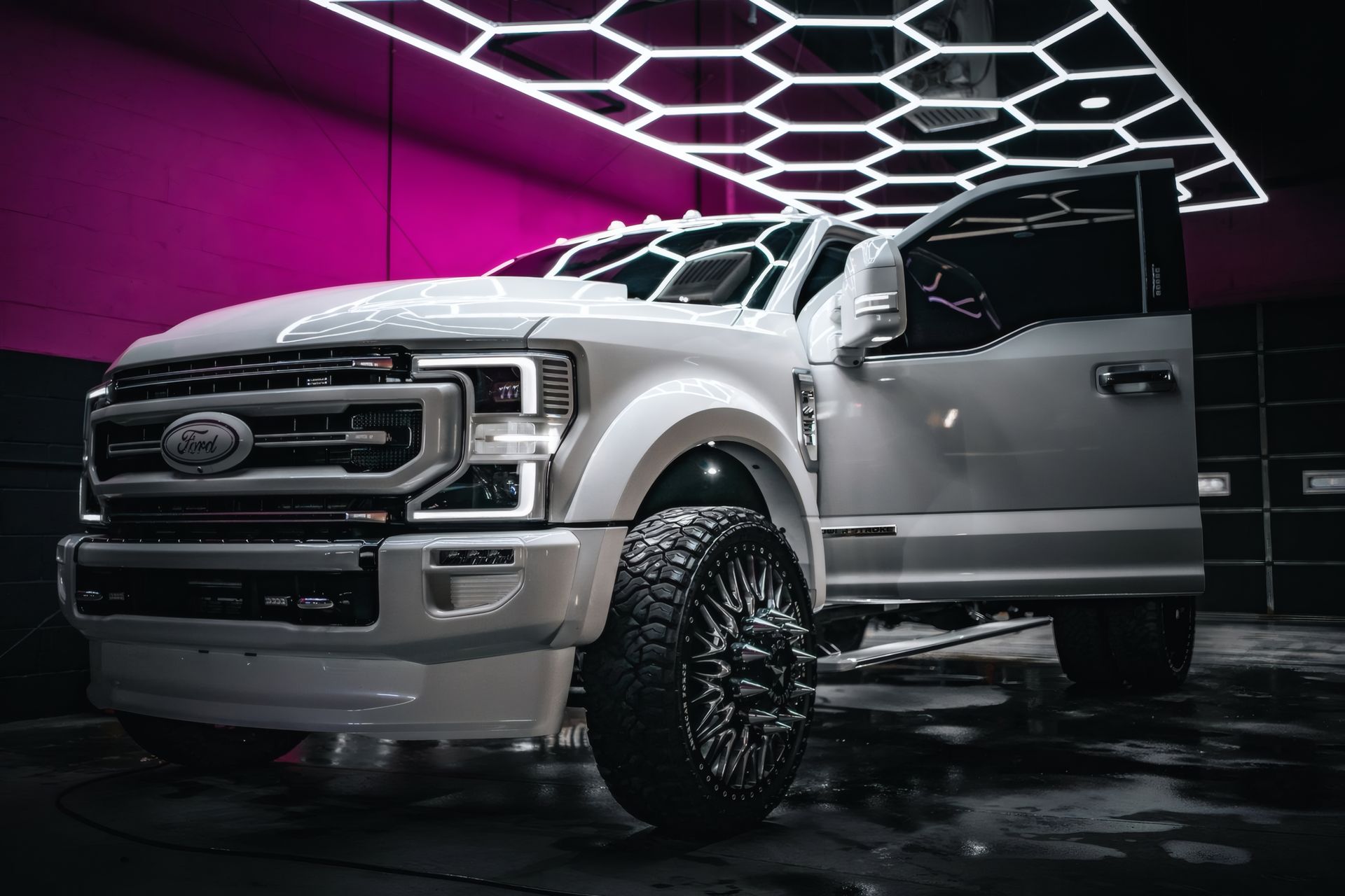 White lifted Ford pickup in a studio with geometric neon ceiling lights.
