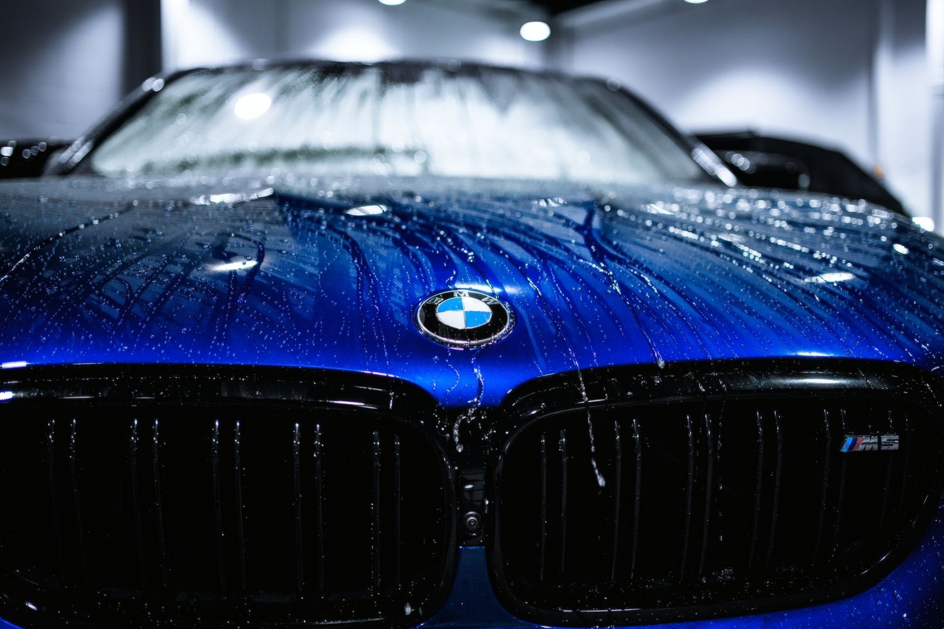 Blue BMW front close-up with water droplets in a dim garage