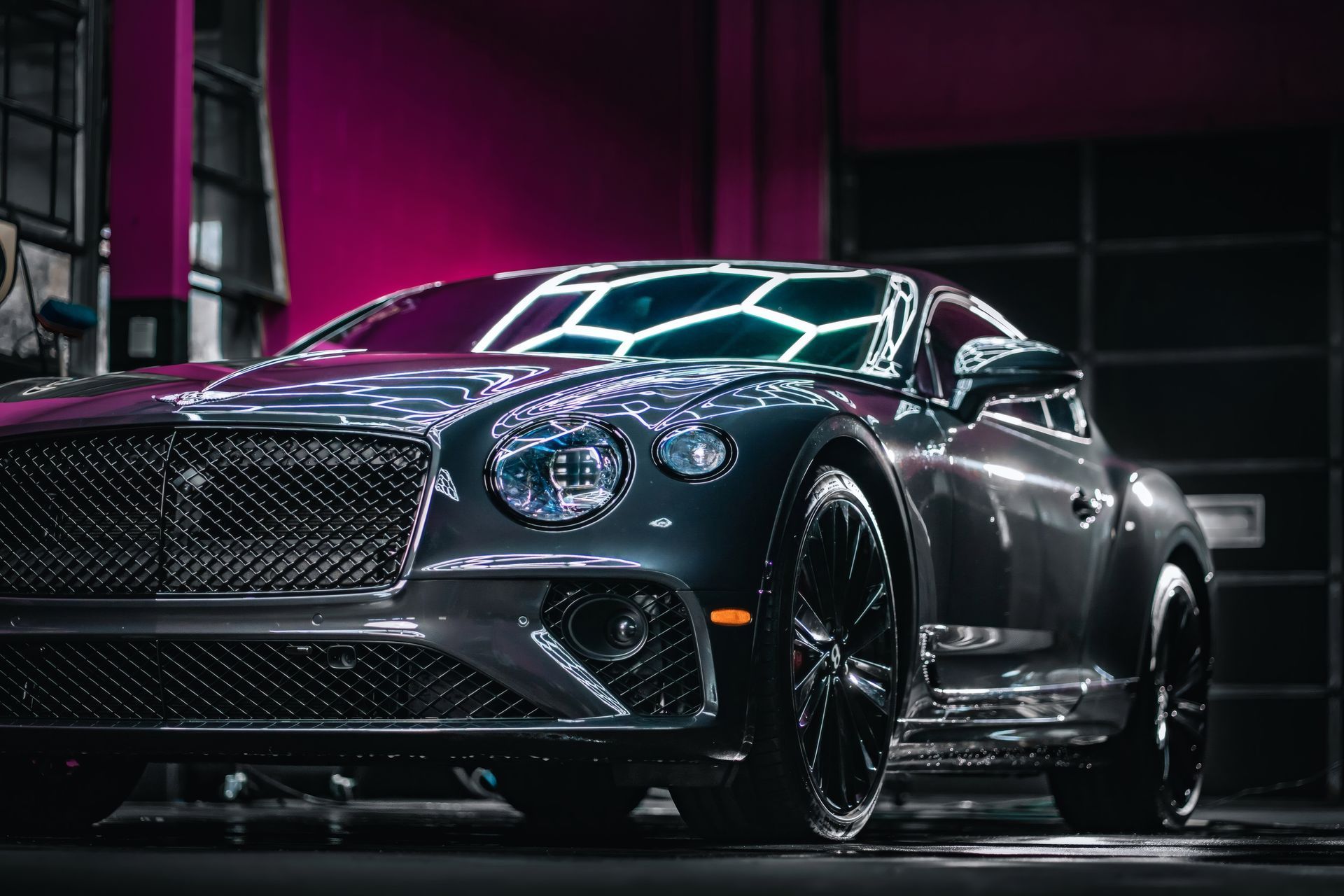 Dark luxury sports car in a neon-lit garage, front angle, glossy black paint and chrome grille