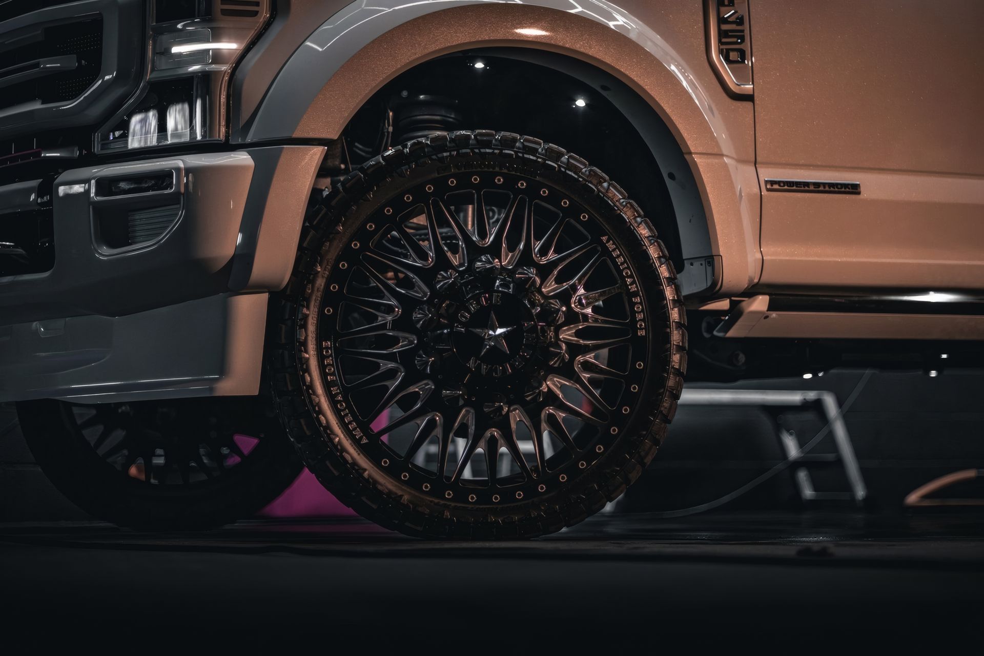 Black custom truck wheel and chrome fender under neon lighting at night