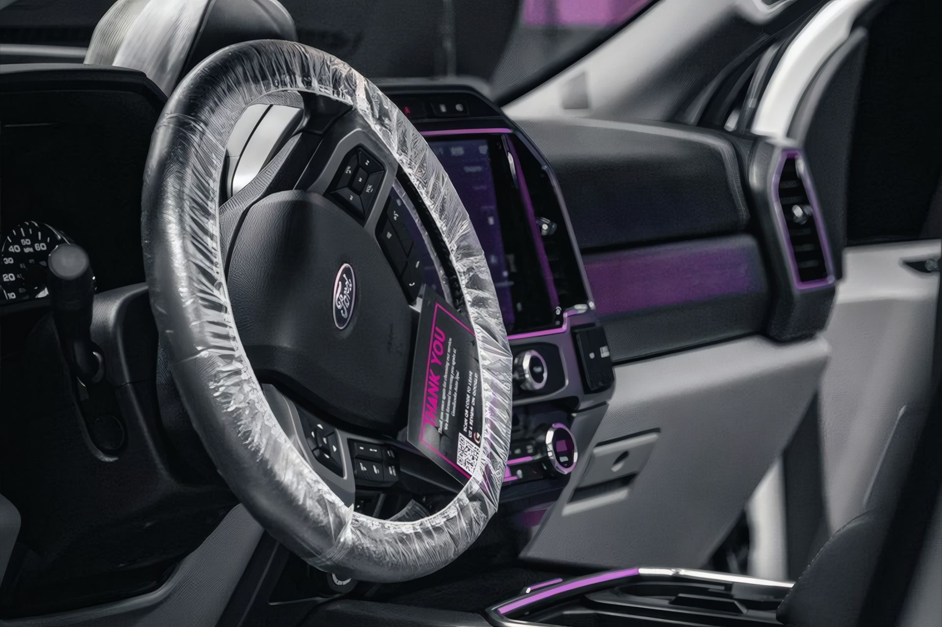 Car interior with a plastic wrapped steering wheel and purple ambient lighting around the dashboard.