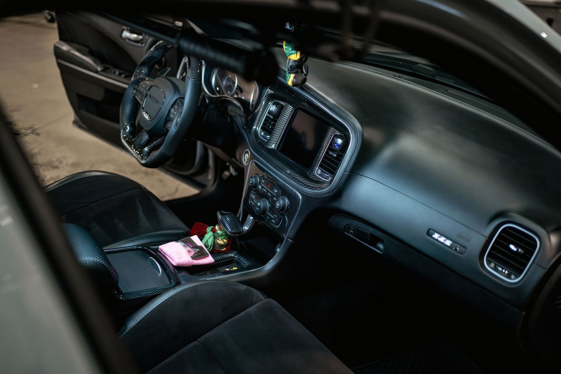 Car interior with a modified steering wheel and center console, black dashboard, and pink items on the console