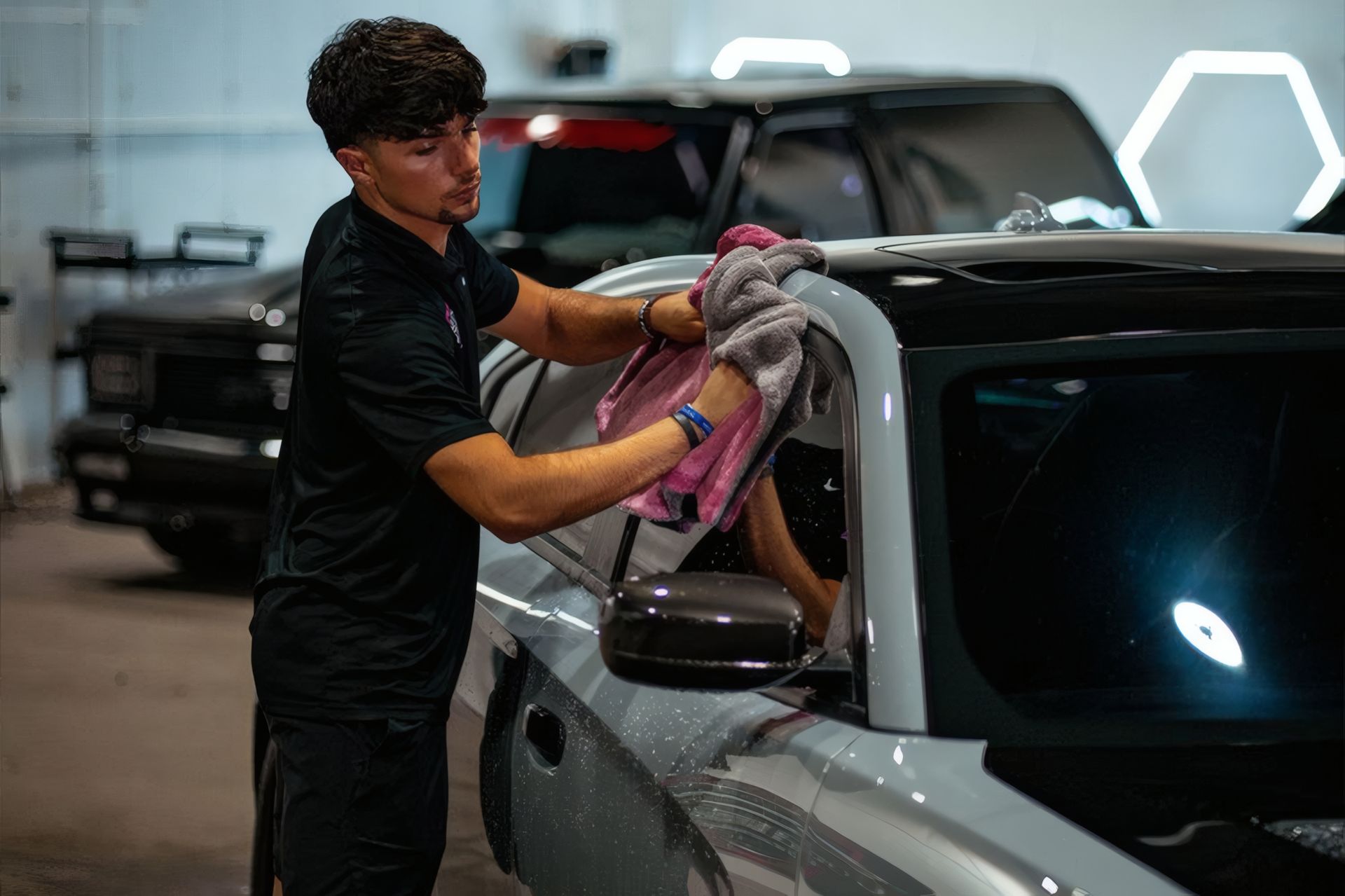 Person wiping a gray car with a cloth in a garage detail shop