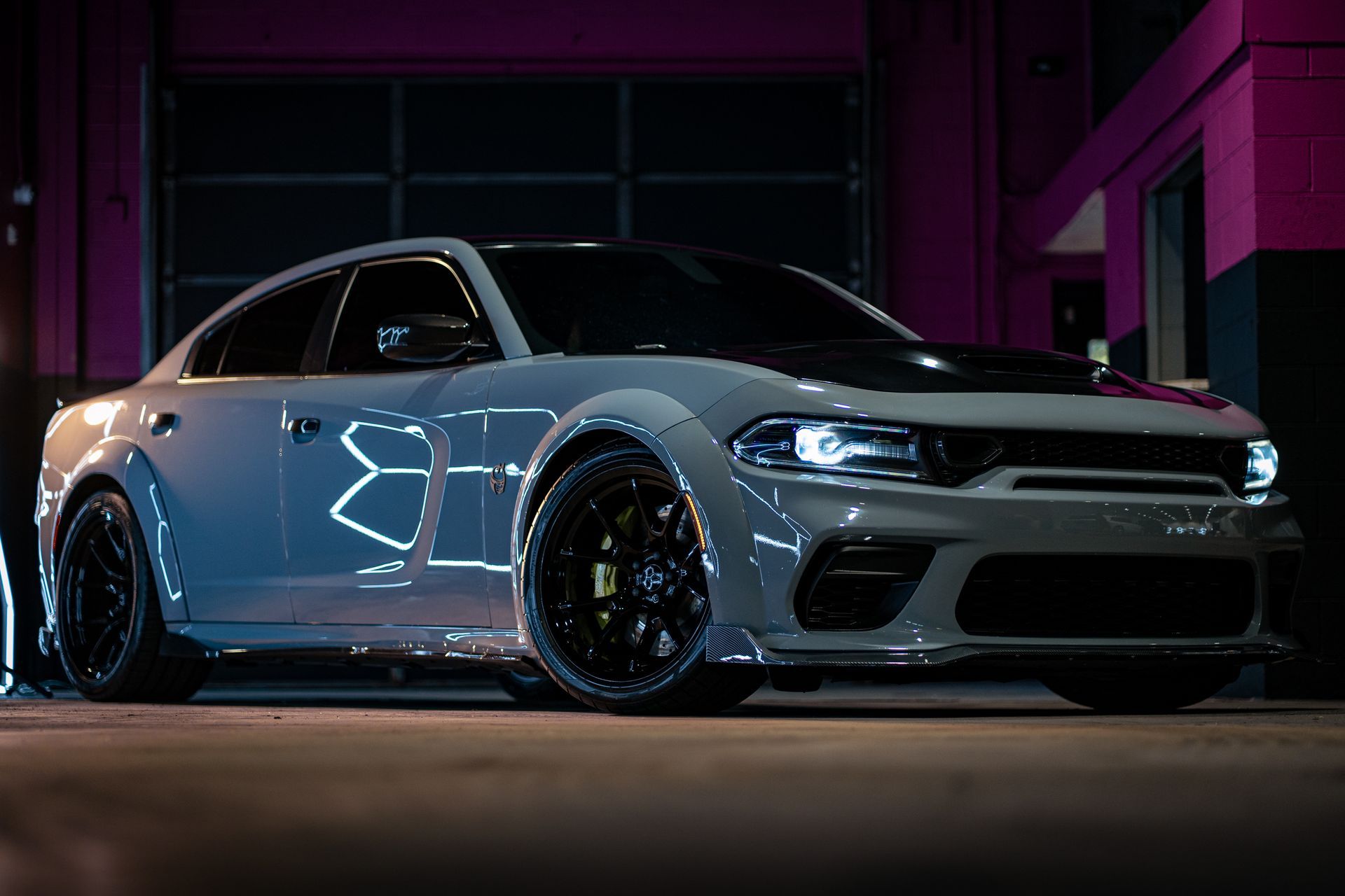 White sports coupe with black hood parked in a dim purple-lit garage