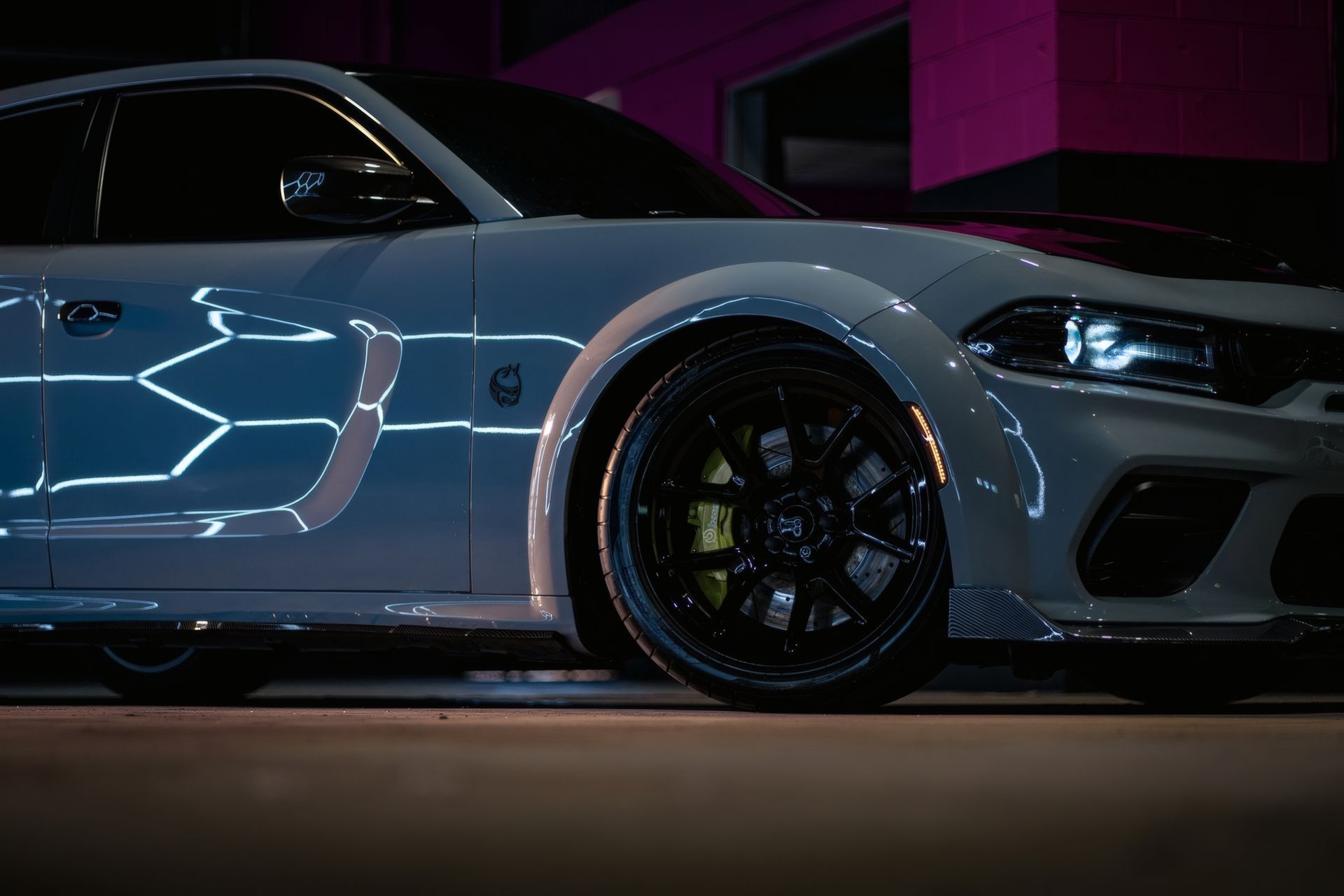 Gray sports car with black wheels parked under neon purple lighting