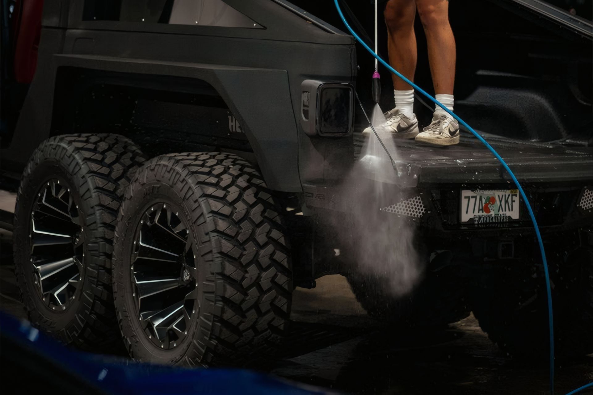 Black off-road truck being pressure washed, with mist spraying over large rugged tires.