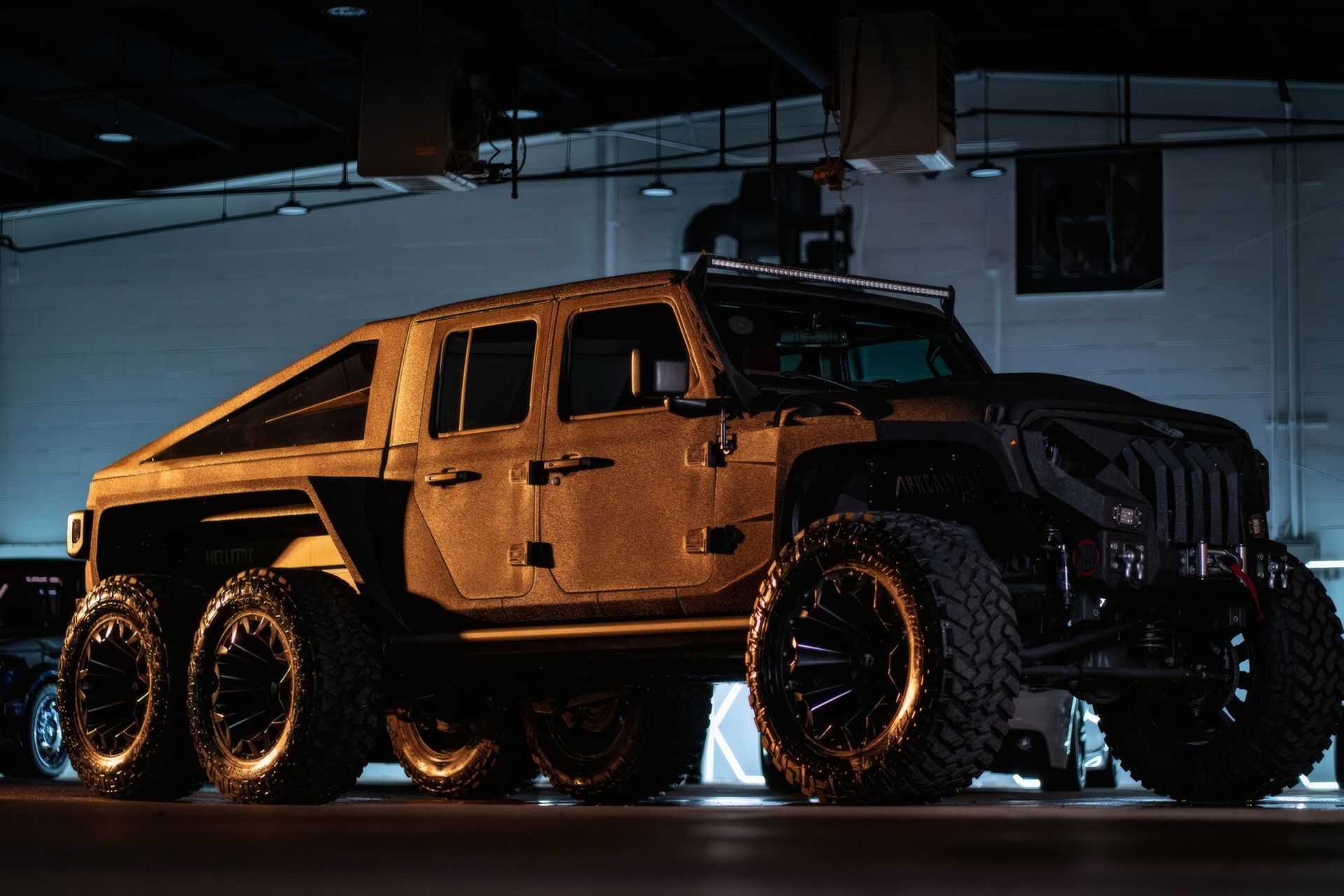 Black six-wheeled off-road truck with orange lighting in a dim garage