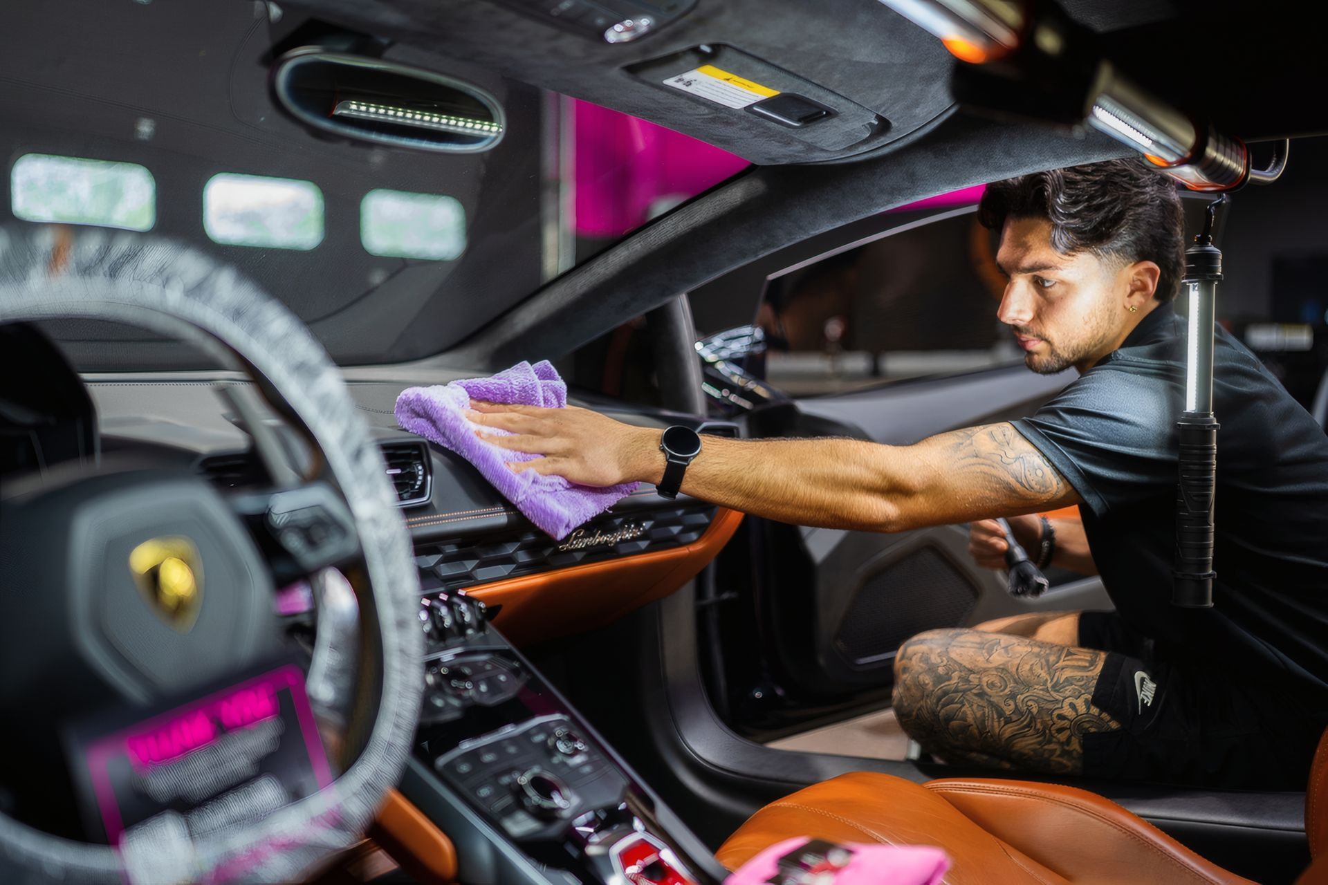 Detailing a luxury sports car interior with a person wiping the dashboard using a purple cloth