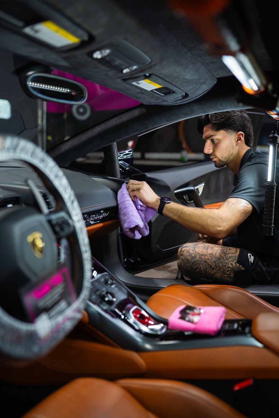 Person washing a gray sports car with a purple cloth in a car wash bay
