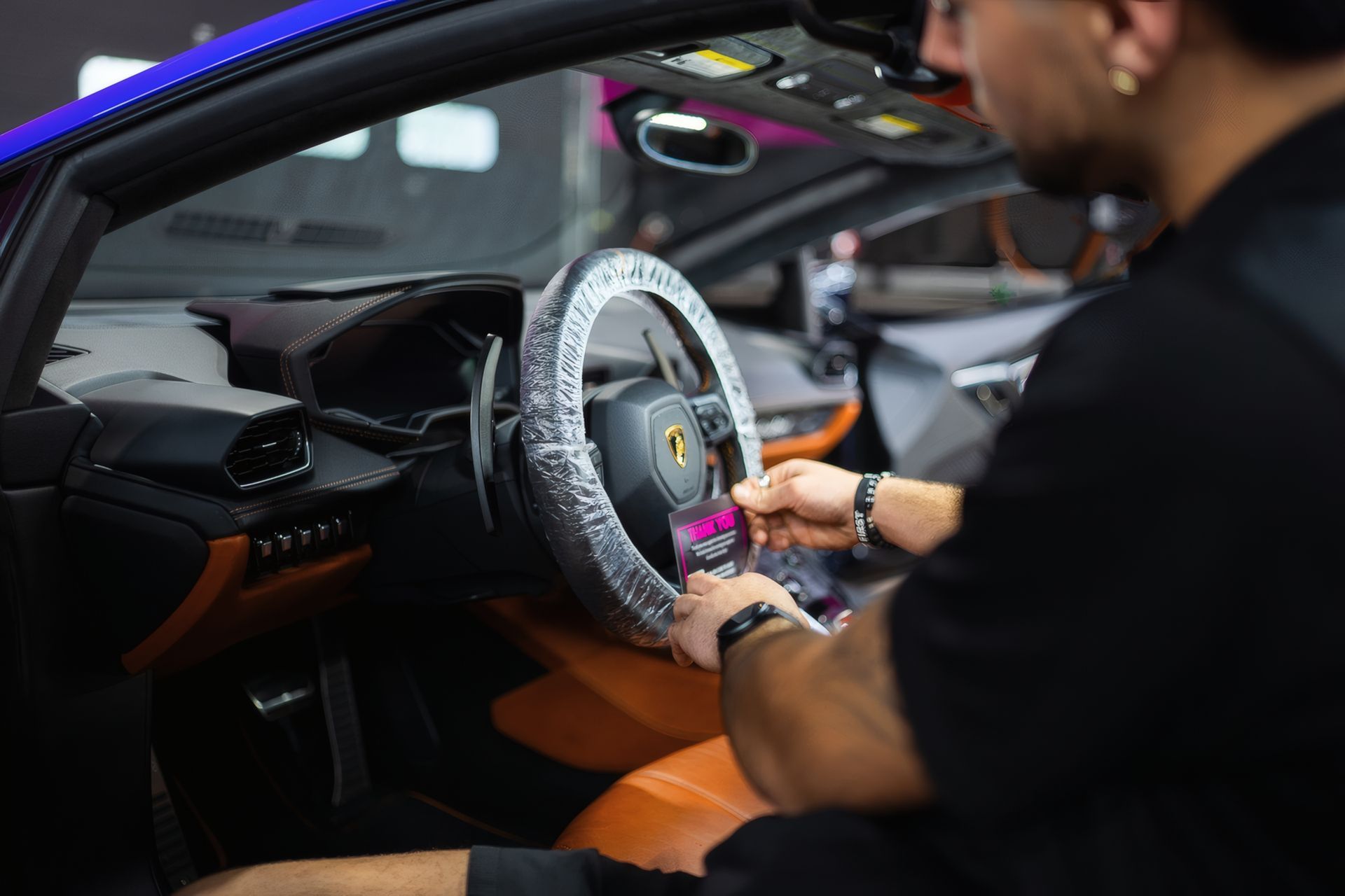 Person installing a gray steering wheel cover inside a car interior with orange seats
