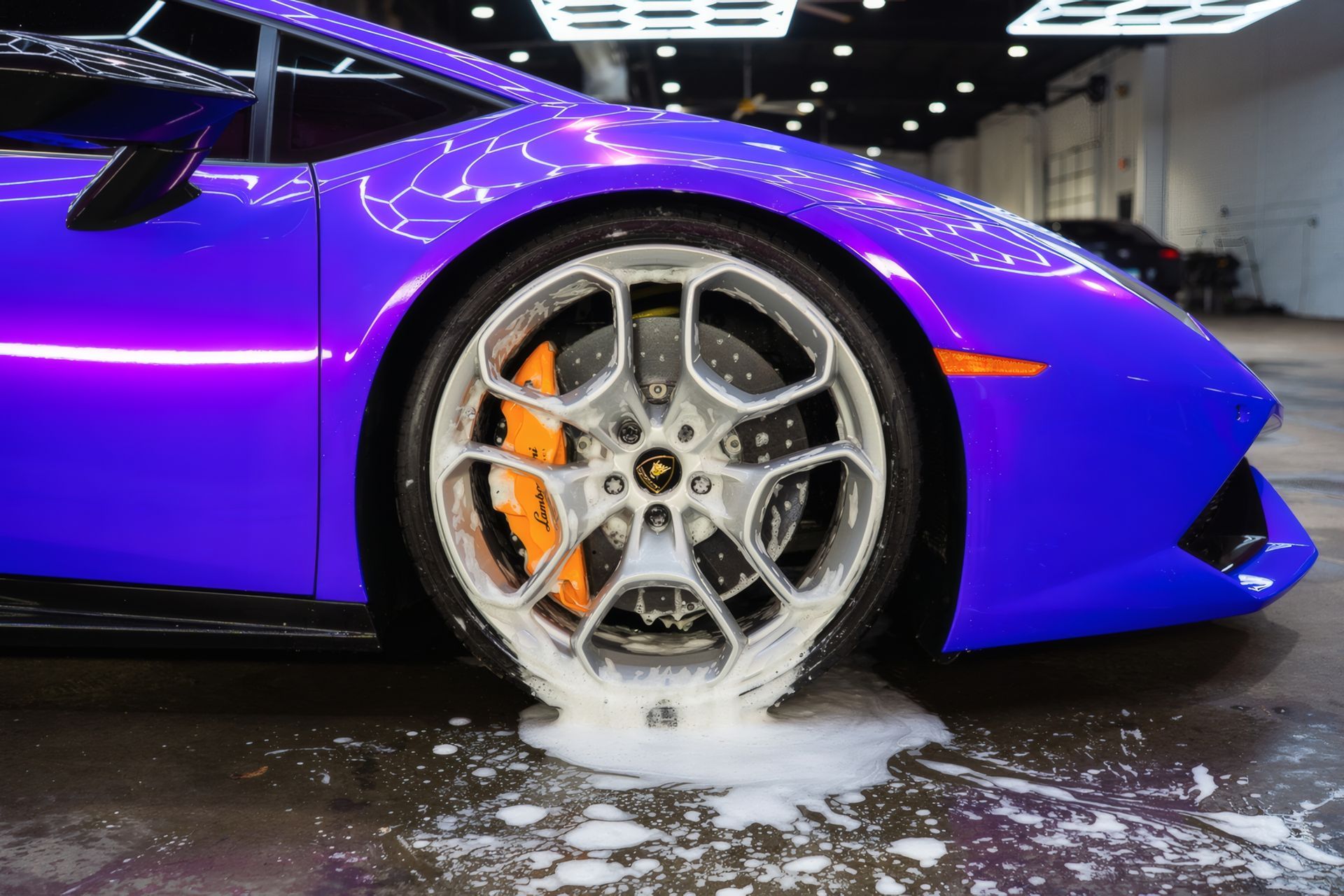 Purple sports car wheel being washed, with soap suds on the floor.