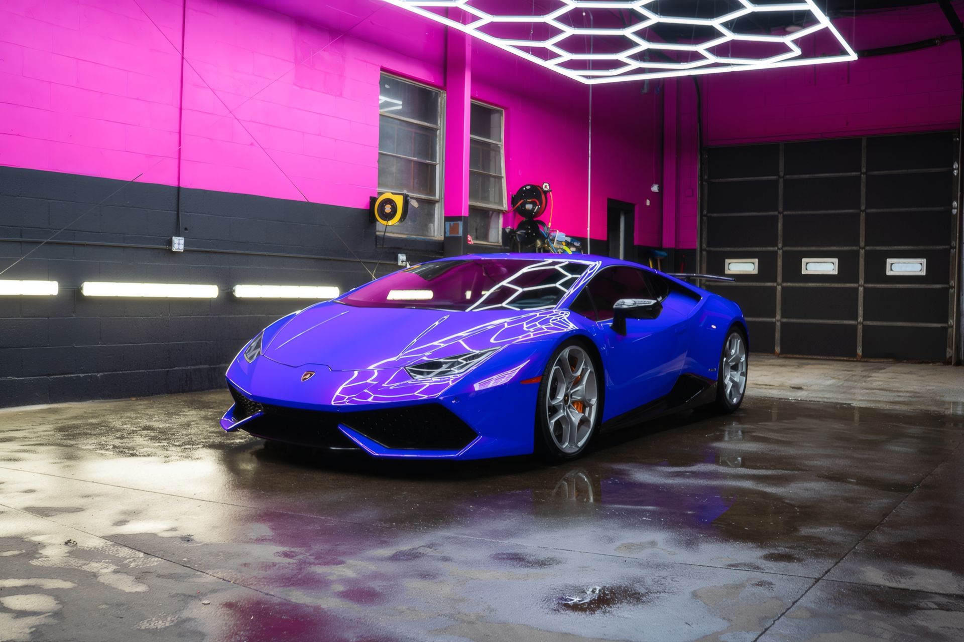 Blue sports car in a neon-lit garage with pink walls and wet concrete floor