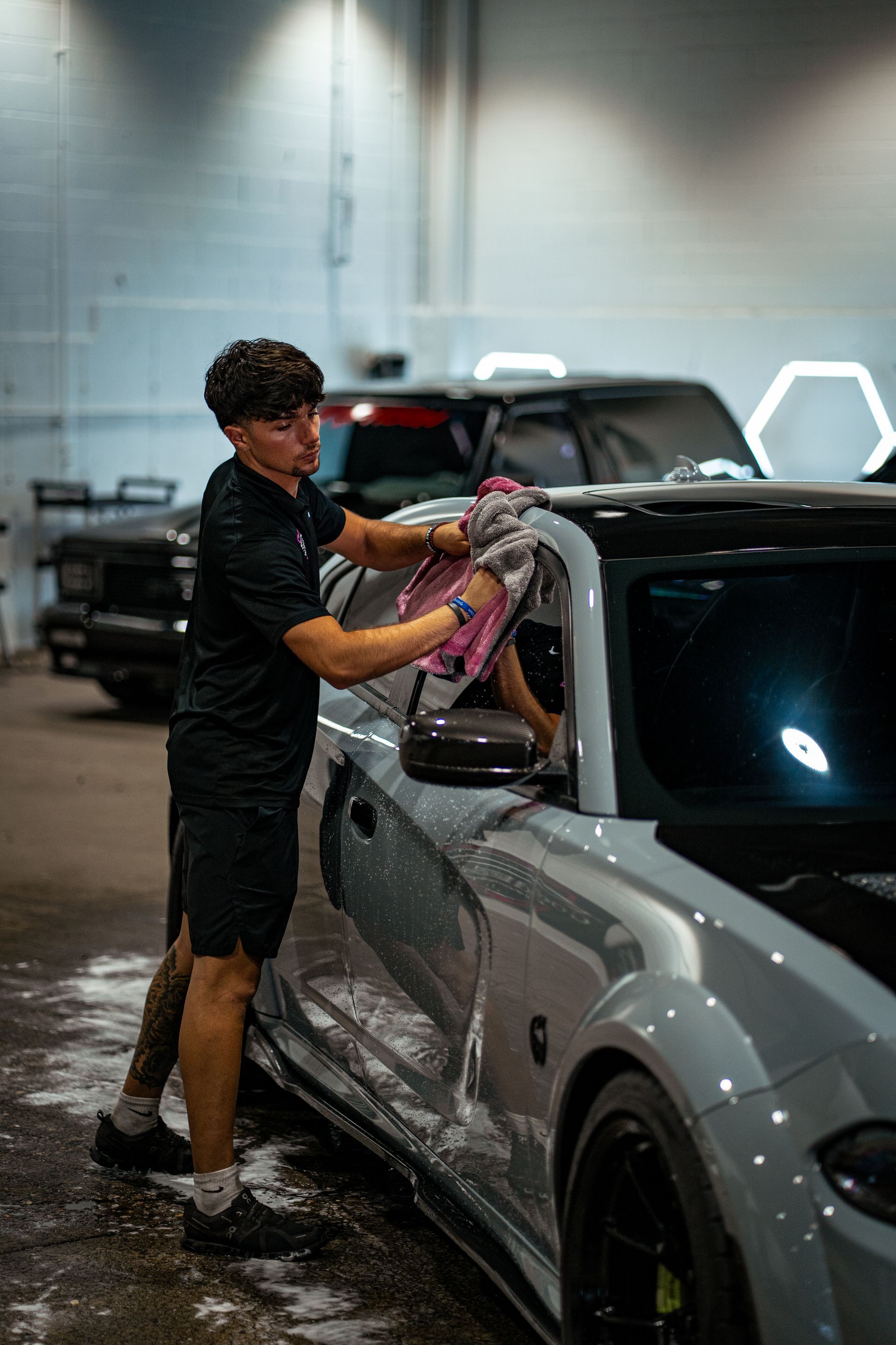Person washing a gray sports car with a purple cloth in a car wash bay