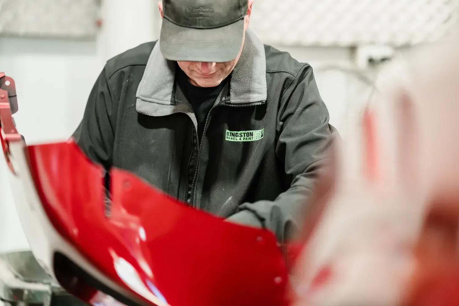 Technician Inspecting a Red Vehicle Part in a Workshop — Kingston Panel & Paint in Huntingfield, TAS