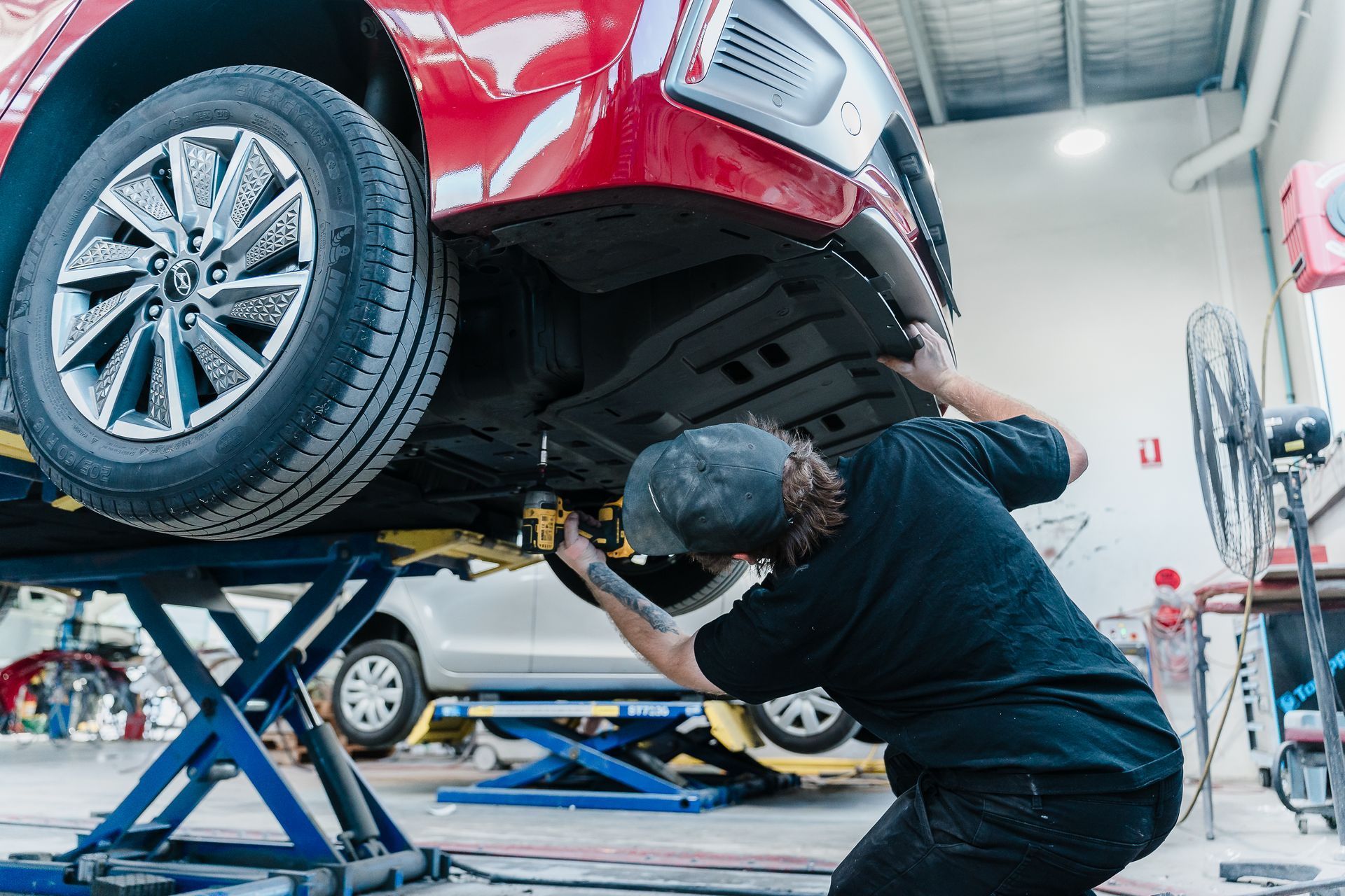 Mechanic Inspecting the Underside of a Red Car on a Lift — Kingston Panel & Paint in Huntingfield, TAS