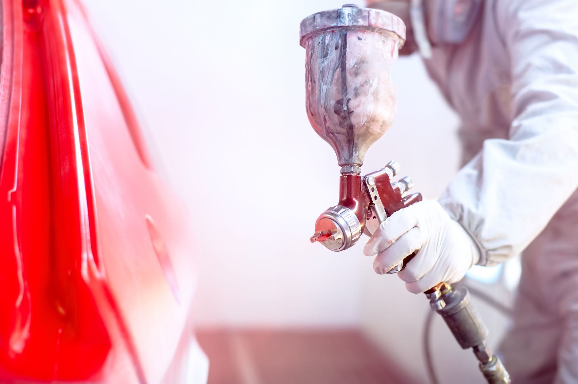 Person Spray-painting a Red Surface With a Paint Gun in a Workshop — Kingston Panel & Paint in Huntingfield, TAS