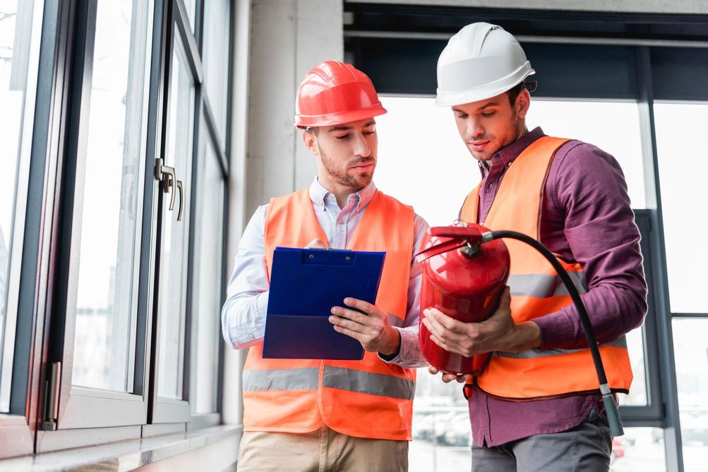 Due operai edili con elmetti e giubbotti di sicurezza consultano un blocco appunti in un cantiere.