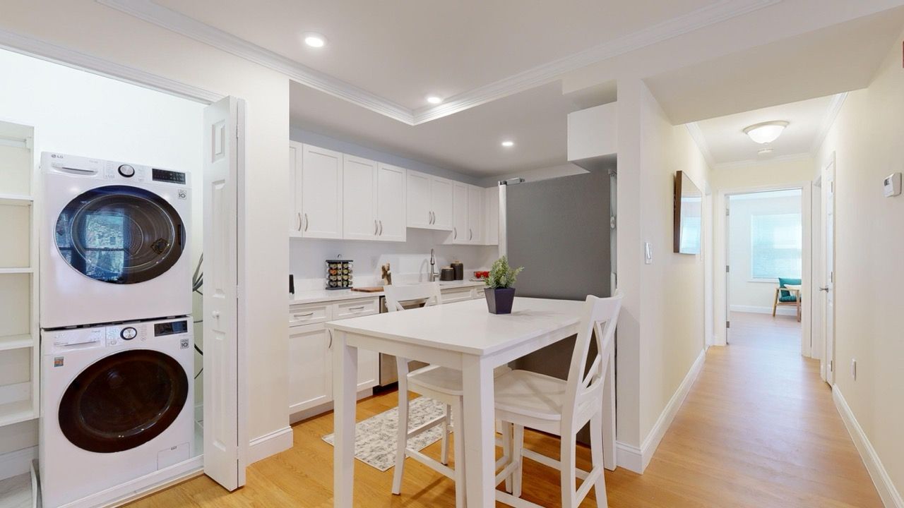 Bright apartment kitchen with white cabinets, island, and stacked washer/dryer near the entry.