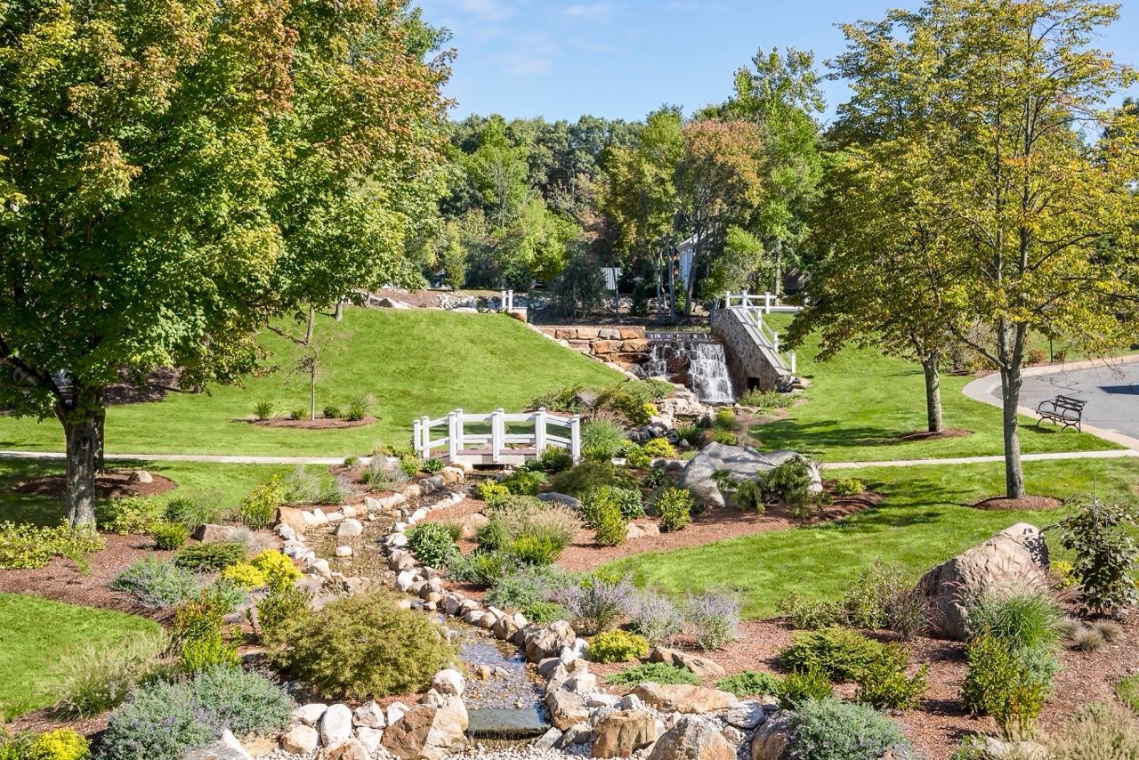 Well-manicured community garden with a small waterfall, bridge, rocks, and benches.