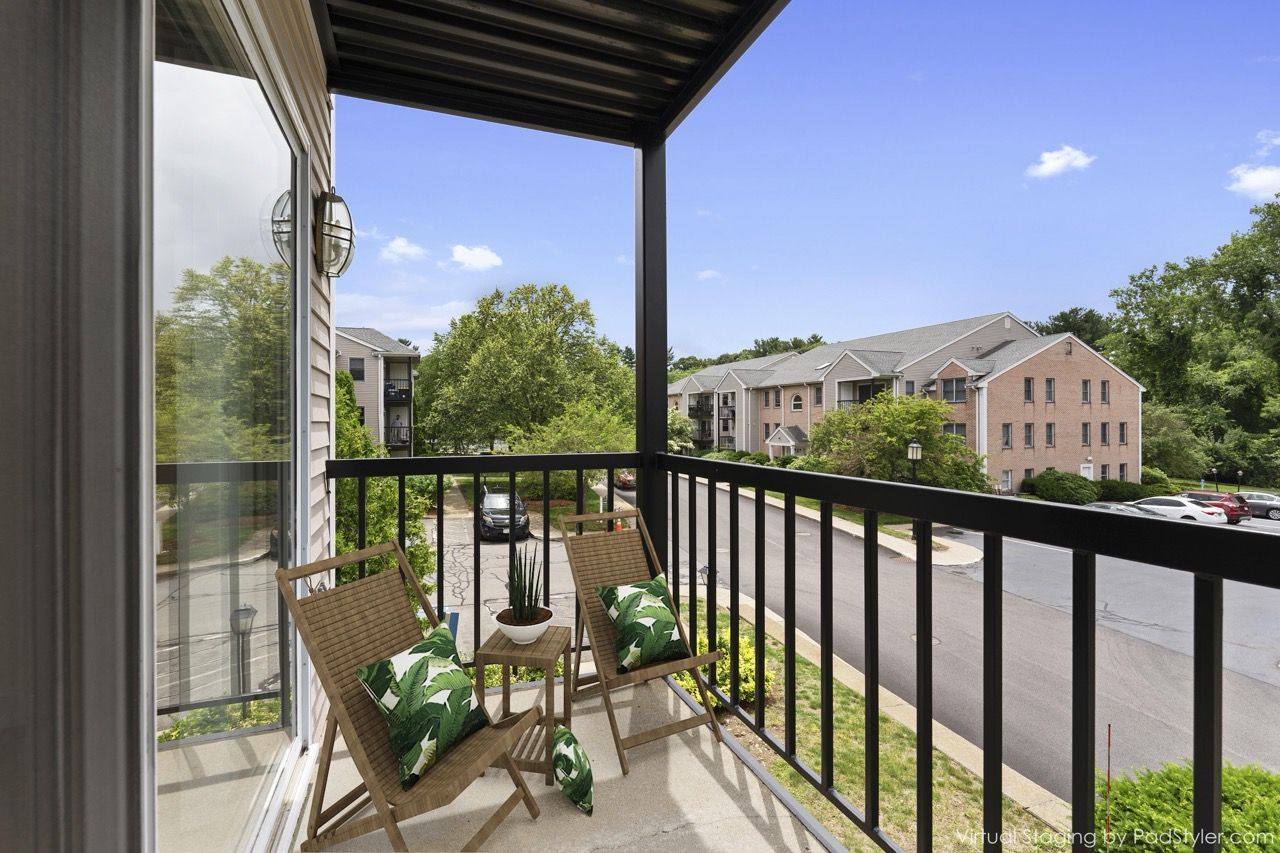 Balcony with two wooden chairs, a small table, and a potted plant, overlooking a street.