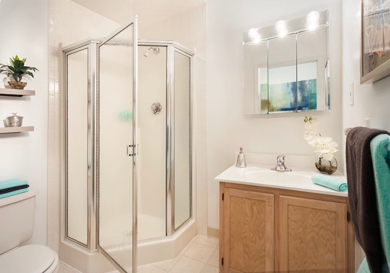Bathroom with a glass shower enclosure, vanity, mirror with lights, and towels.