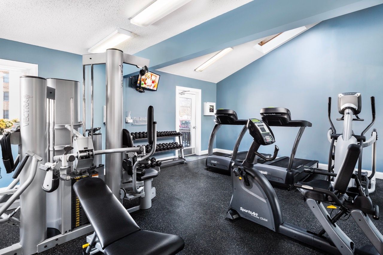 Inside a resident gym with blue walls, featuring treadmills, a stationary bike, and weight machines.