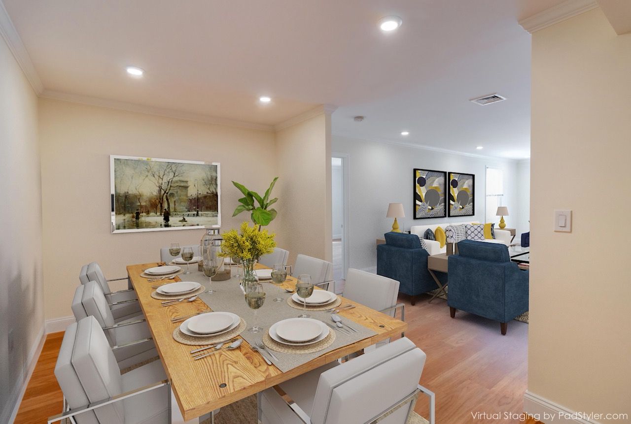 Open-concept dining room with a wooden table, white chairs, and a connected living area with blue sofas.