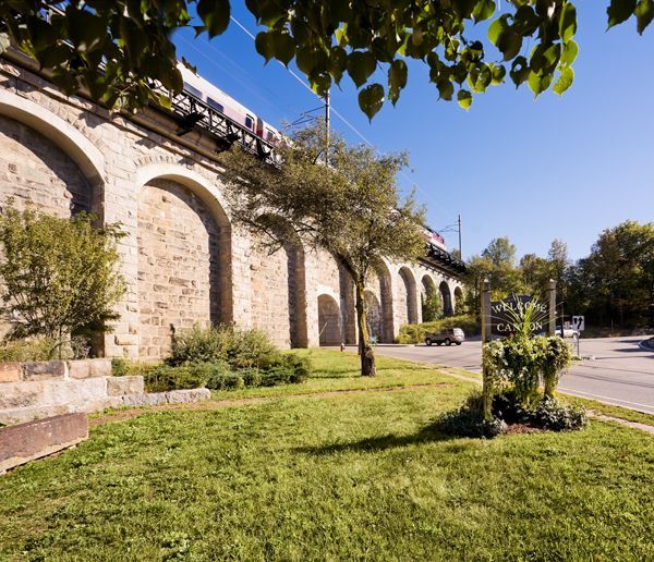 Stone viaduct with arches beside a green lawn and trees under a clear blue sky