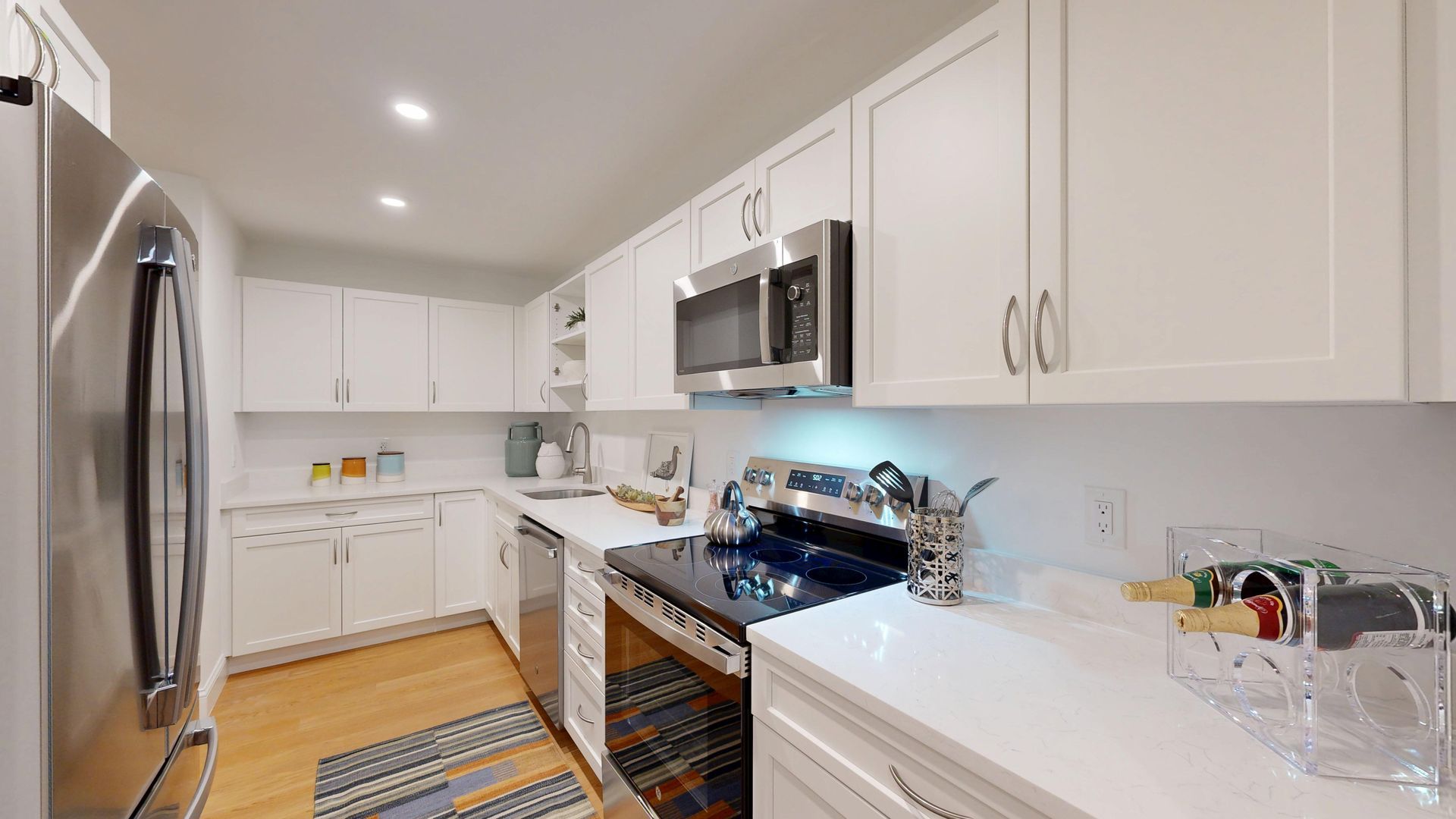 Bright modern kitchen with white cabinets, stainless steel appliances, and a patterned rug on the floor