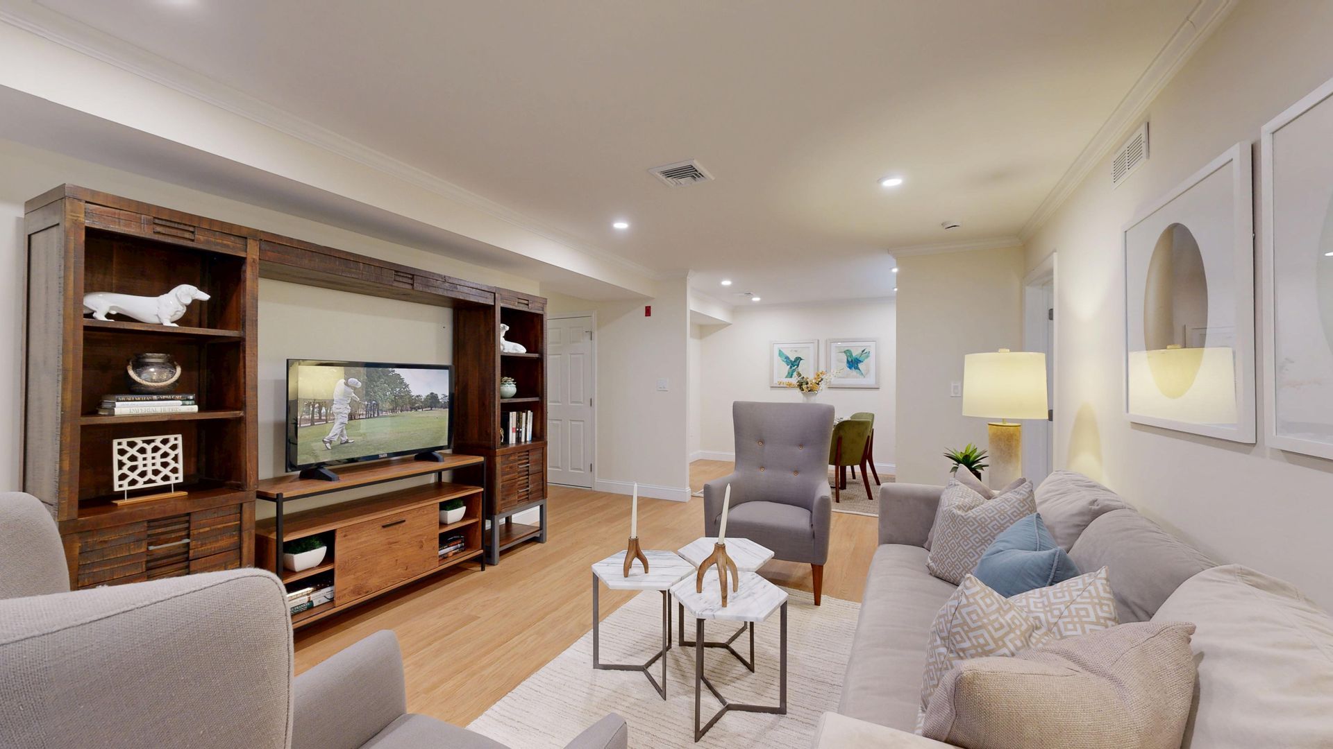 Modern living room with TV wall unit, beige sofa, armchairs, coffee tables, and warm lighting
